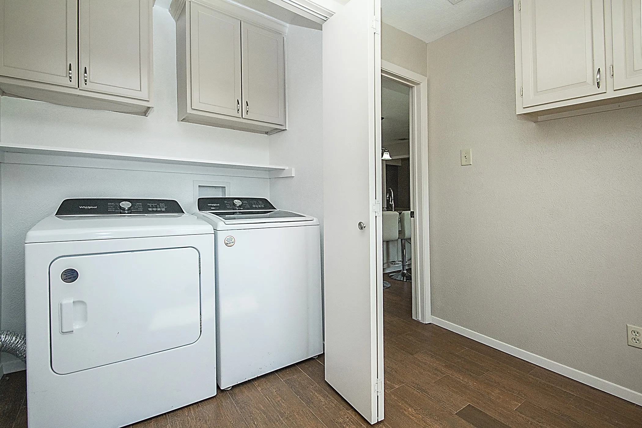 Wood-finish flooring with light-toned walls, built-in upper cabinetry, and a wall-mounted shelving unit