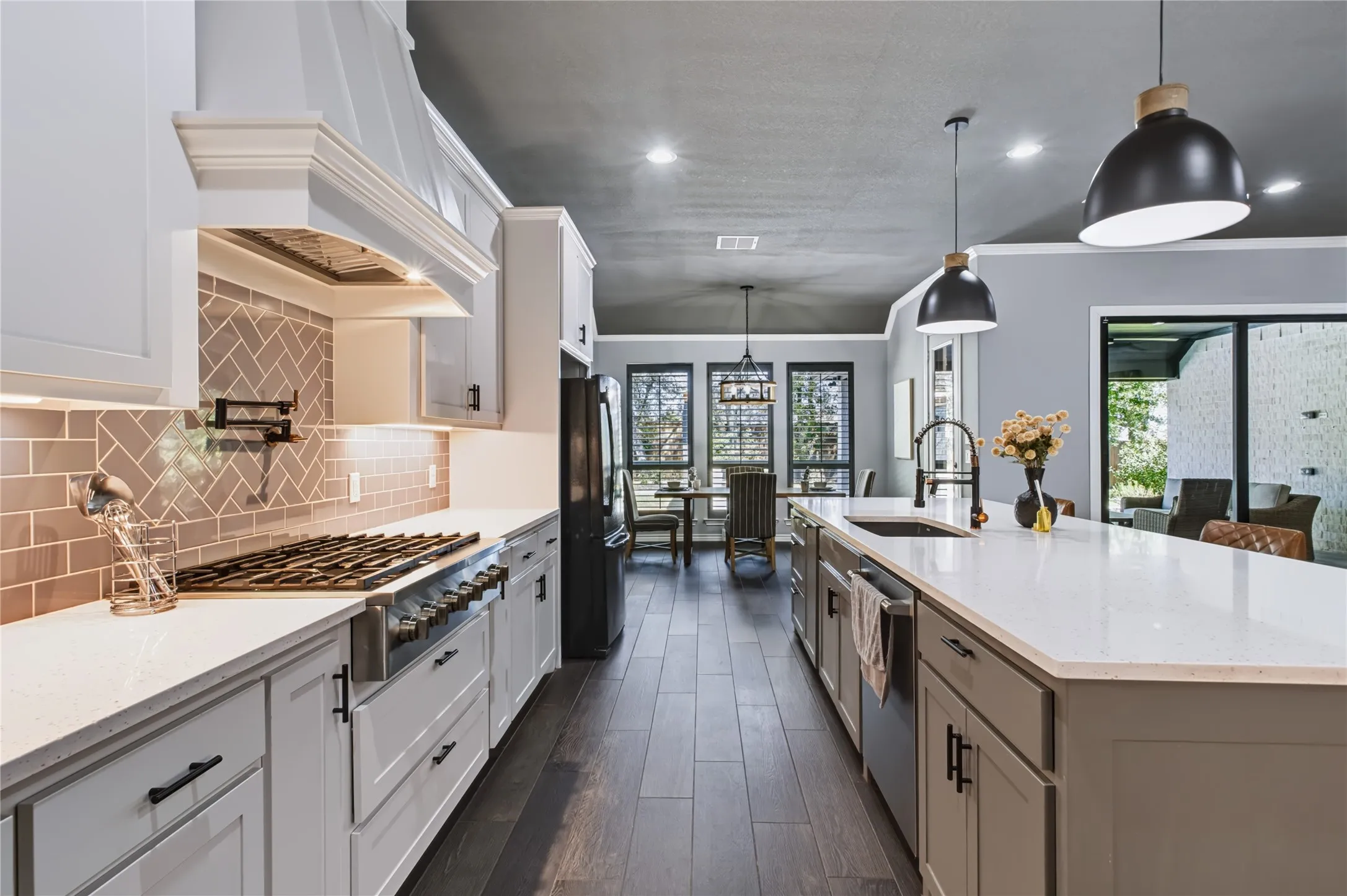 Chef's kitchen featuring white cabinetry, stainless steel gas range and dishwasher, quartz countertops, herringbone tile backsplash, and a large center island with waterfall edge