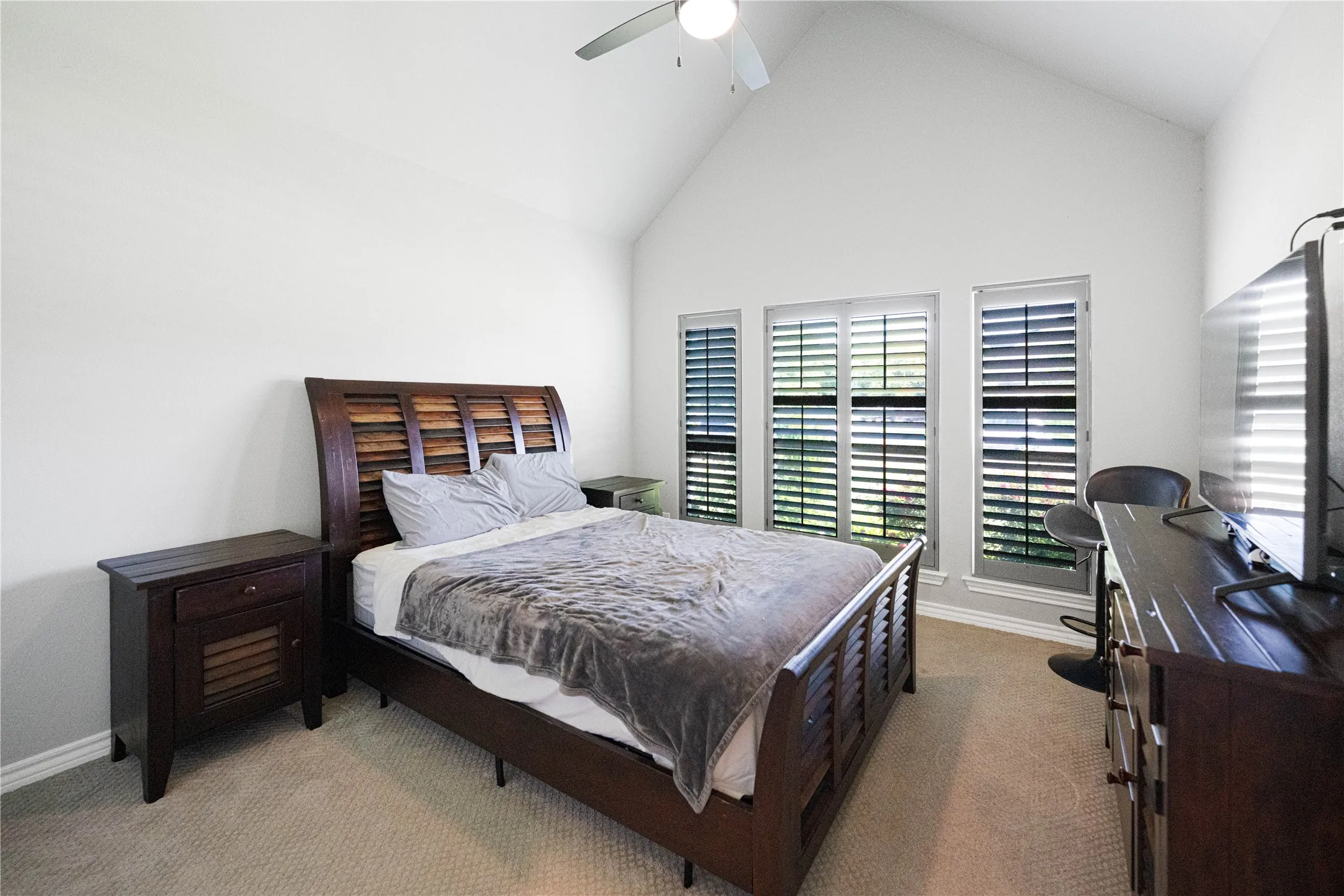 Vaulted ceiling, carpeted flooring, three windows with plantation shutters, ceiling fan