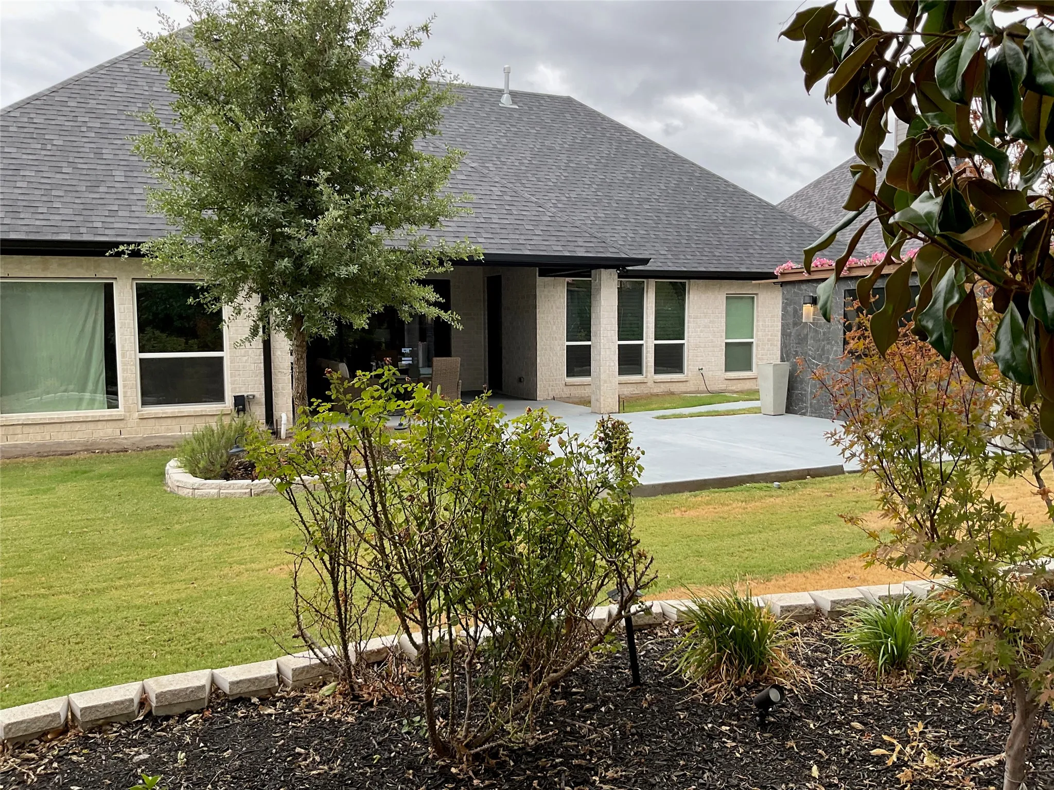 Expansive backyard featuring a manicured lawn, concrete patio, and mature landscaping