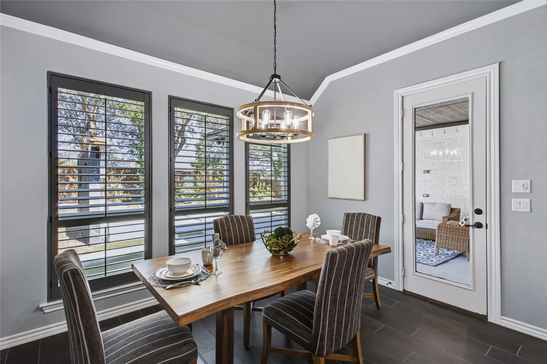 Dining area featuring dark wood-finish flooring, a tiered chandelier with exposed bulbs, and multiple windows with plantation shutters