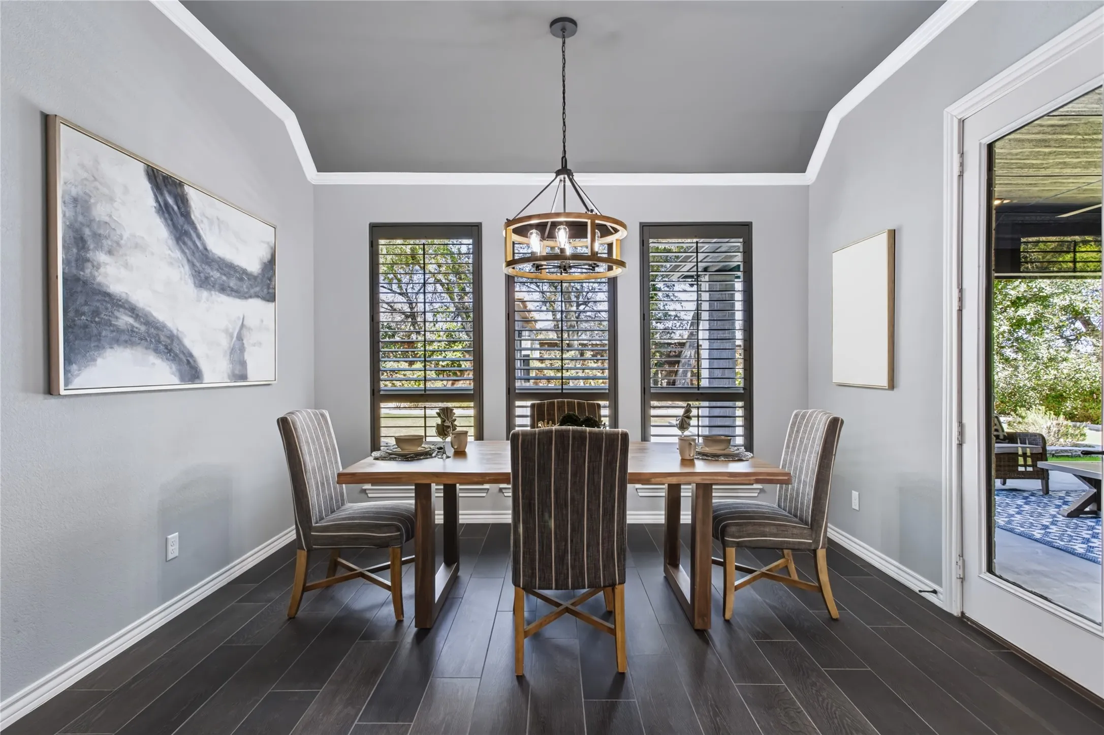 Tray ceiling with crown molding, wood-finish flooring, three windows with plantation shutters, and a wood-frame chandelier
