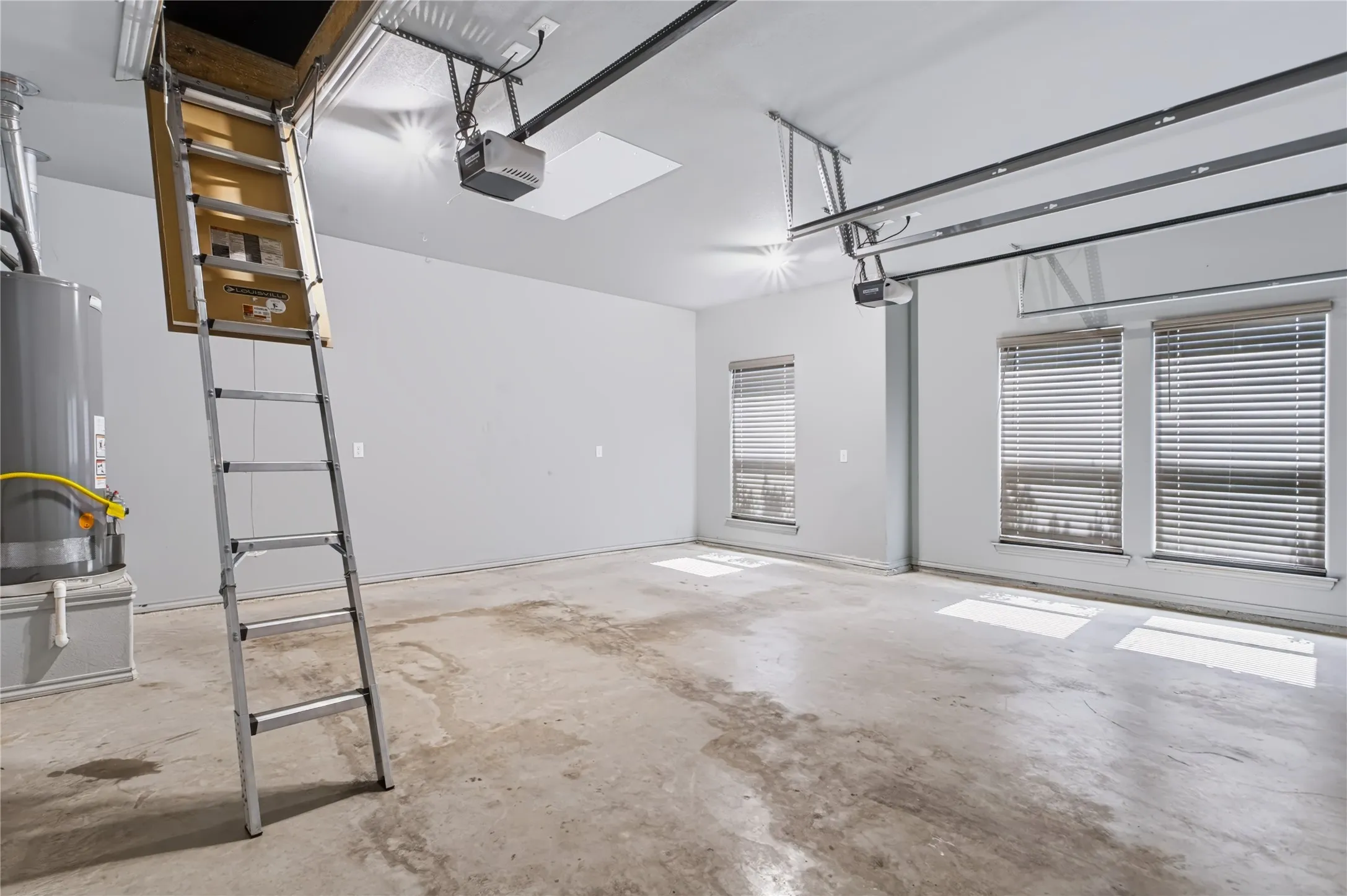 Spacious garage with multiple windows, overhead lighting, and an attic access ladder