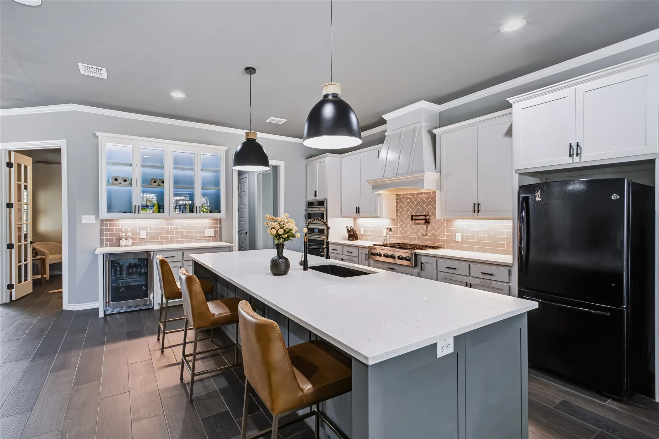 Gourmet kitchen featuring white cabinetry with black hardware, a large center island with white quartz countertop and seating for multiple diners, stainless steel appliances including a professional-style range hood, pendant lighting, and wood-finish flooring throughout