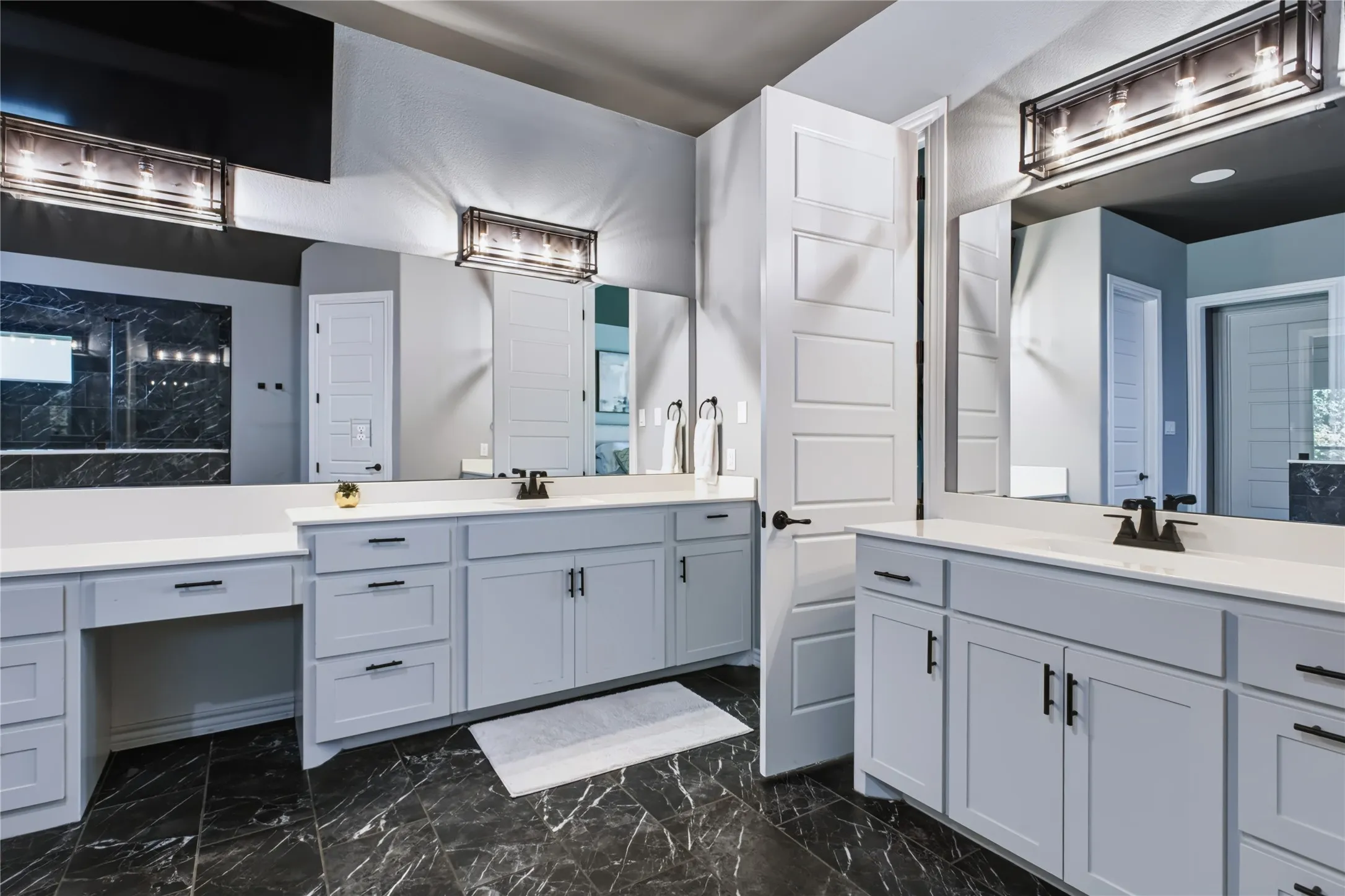 Dual vanity with light gray cabinetry, white countertops, black-finish hardware, and dark marble-look flooring