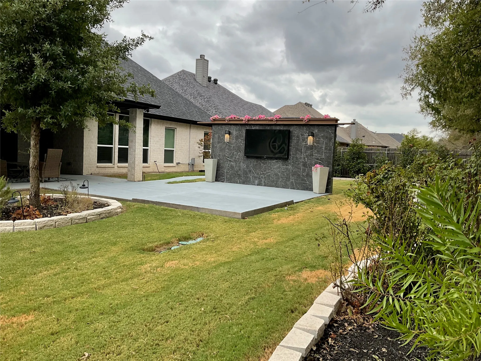 Expansive backyard featuring a stone-clad outdoor entertainment structure, multiple concrete patio areas, and established landscaping