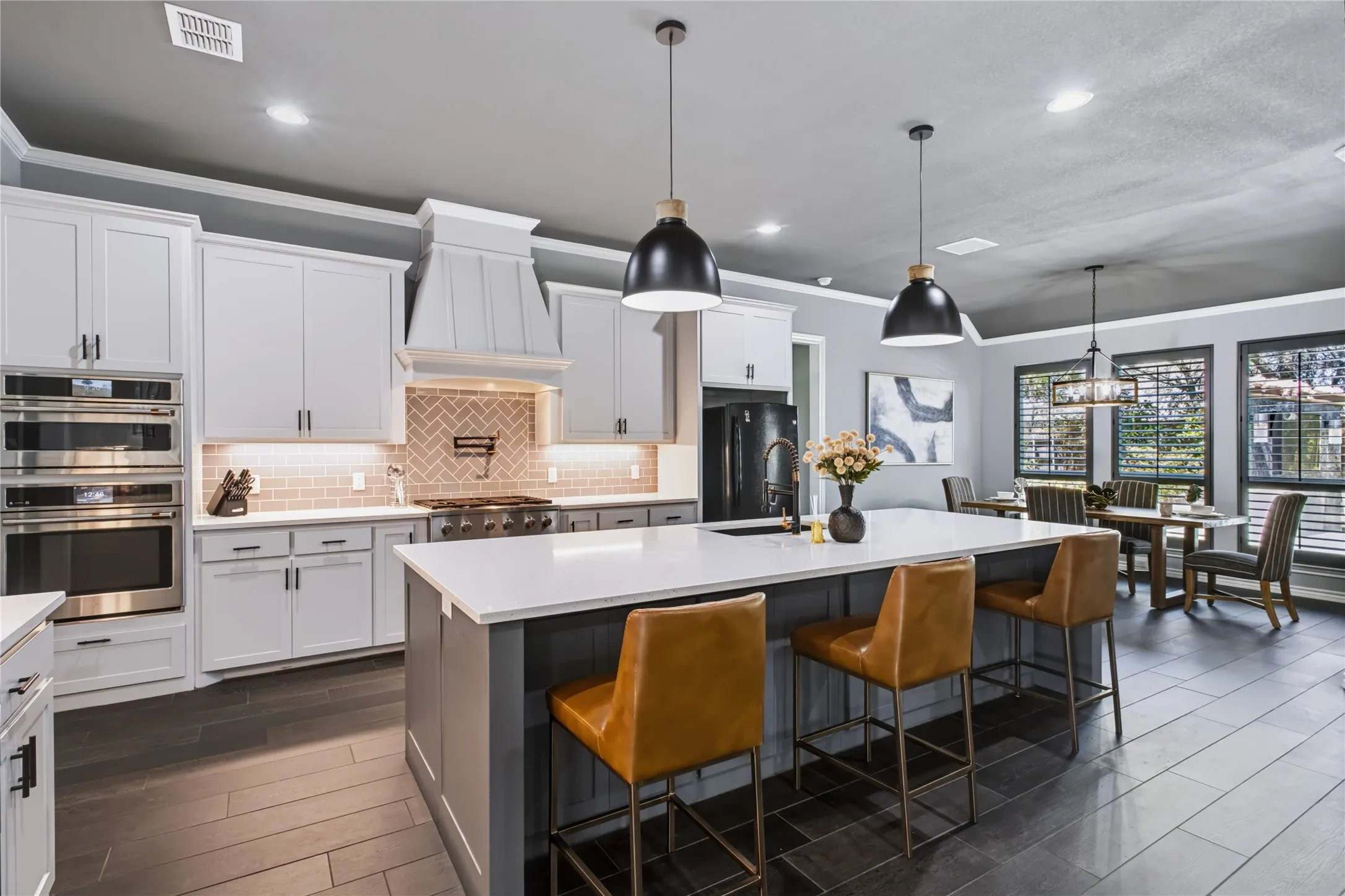 Kitchen featuring white shaker cabinetry, stainless steel appliances, a center island with a sink, and pendant lighting