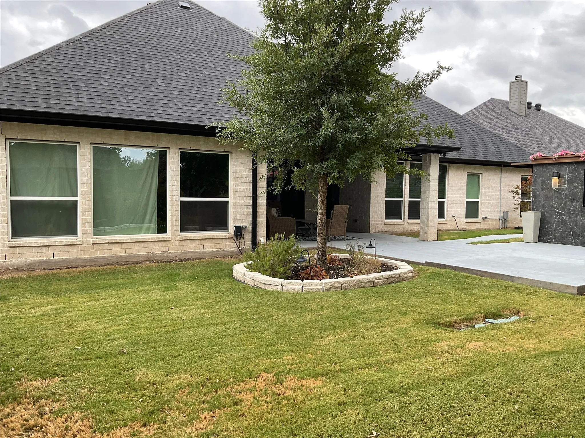 Expansive lawn area with a stone-edged planter, a paved patio, and a covered outdoor living space