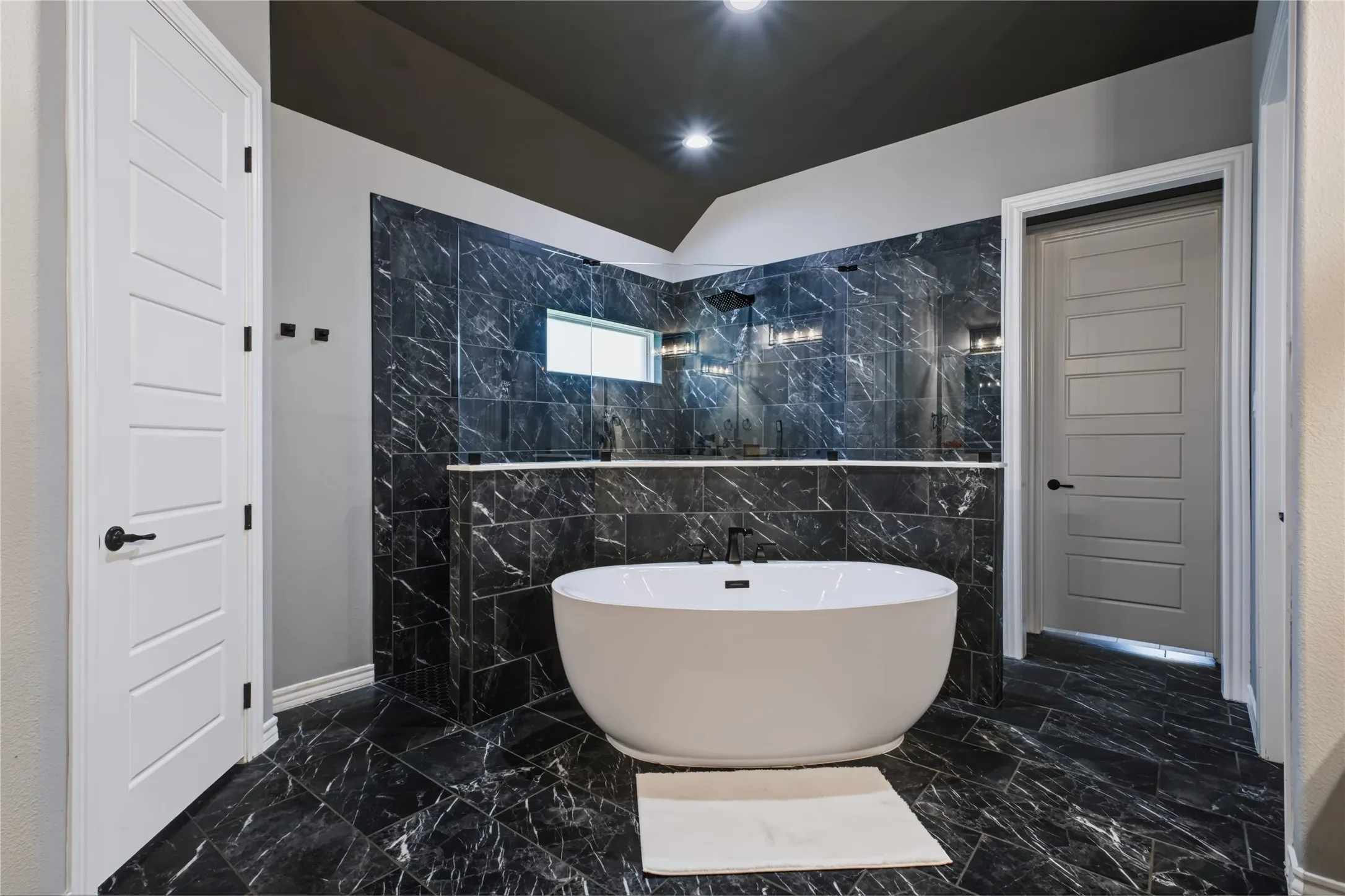Freestanding soaking tub, black tile flooring, black tiled shower with glass enclosure, white paneled doors, and recessed lighting