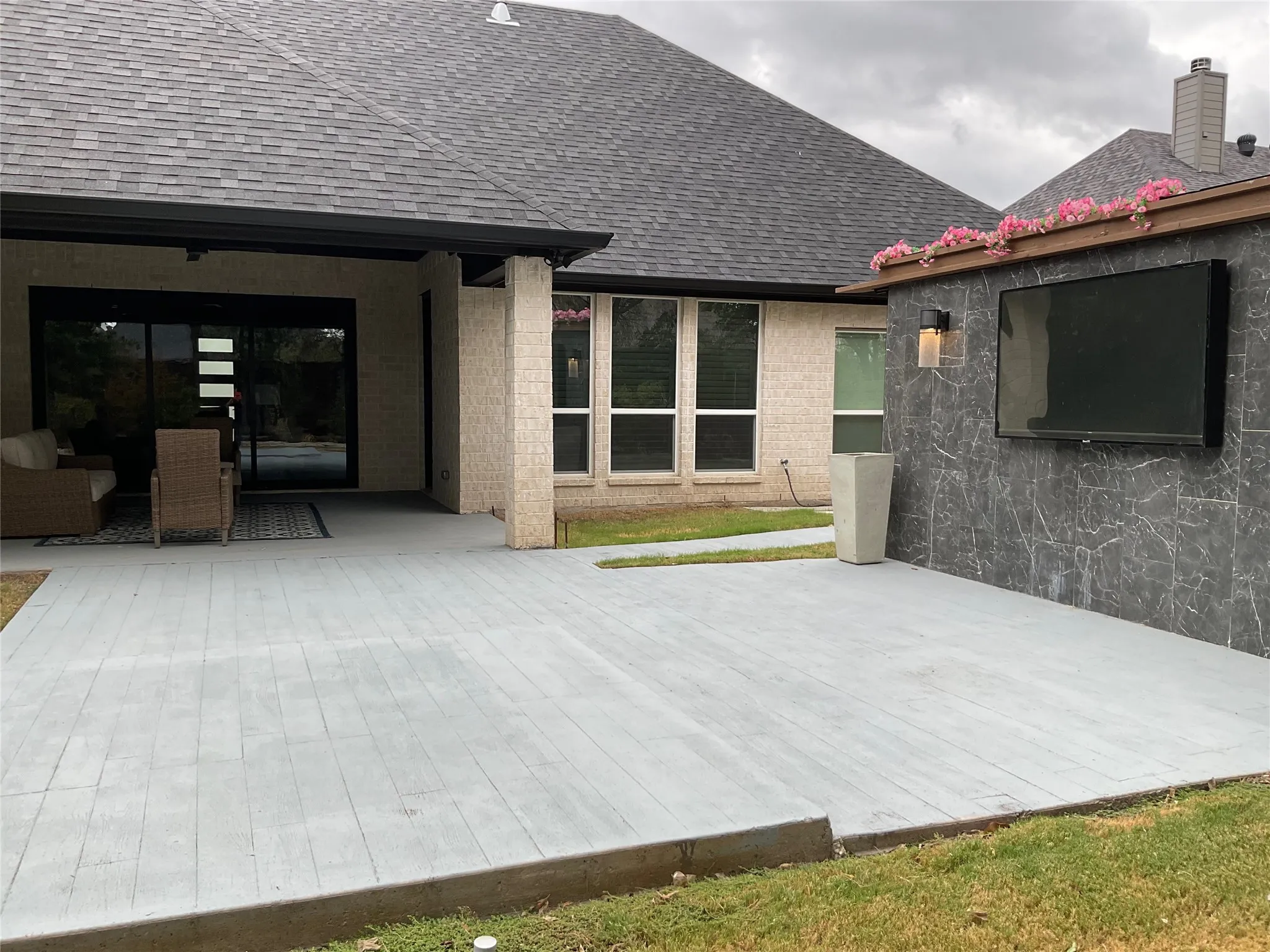 Expansive concrete patio with wood-look finish, protected by a covered section and a dark shingled roof