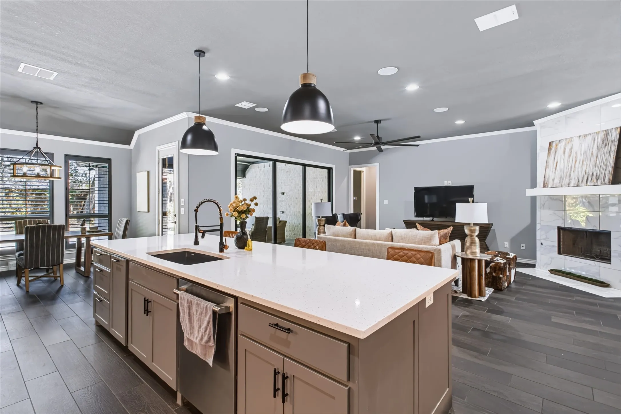 Kitchen island with a white countertop and integrated sink, dark wood-finish flooring throughout, recessed ceiling lighting, and a white tile fireplace surround