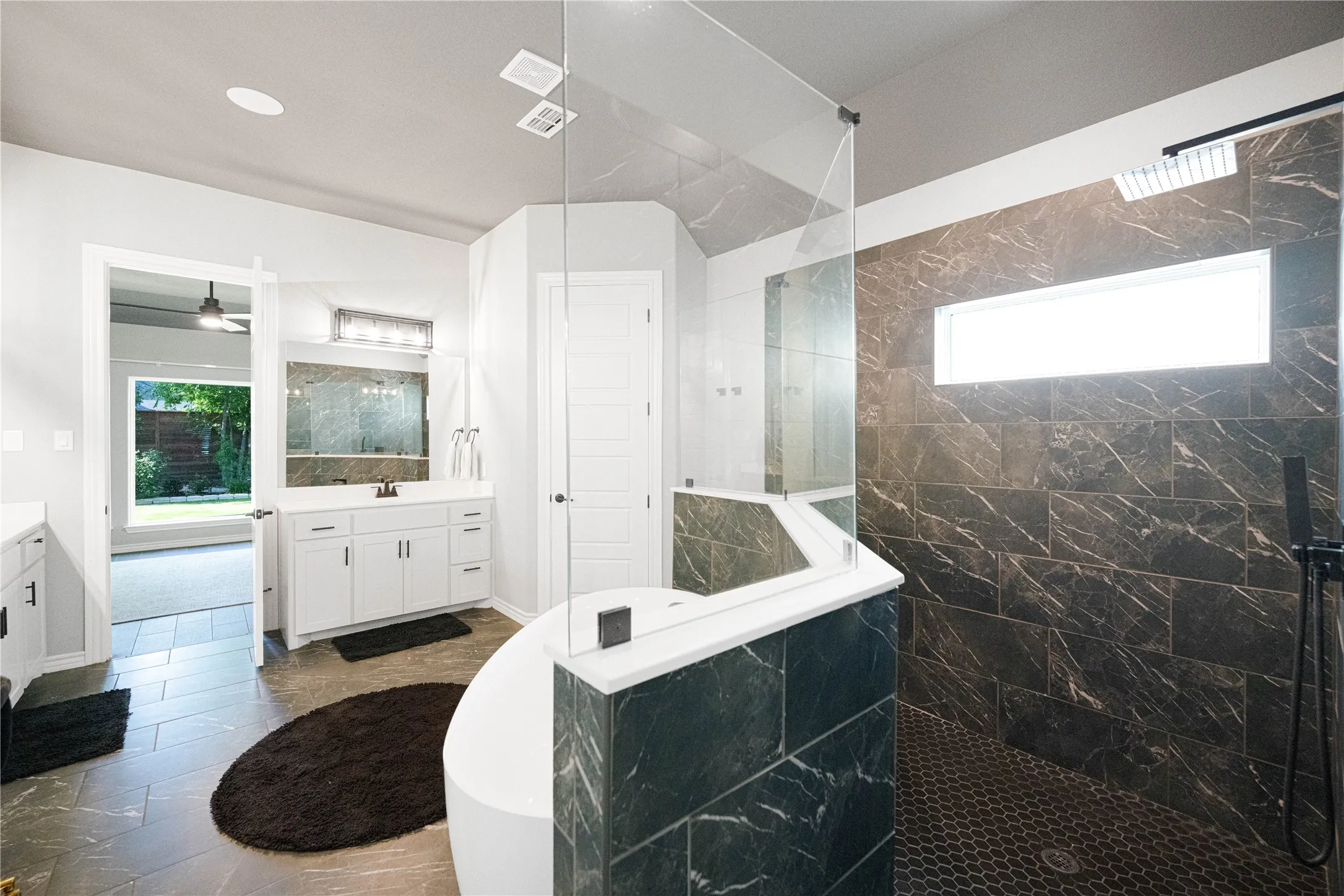 Freestanding soaking tub, walk-in shower with dark marble-patterned tile, frameless glass shower enclosure, and a double vanity with white cabinetry