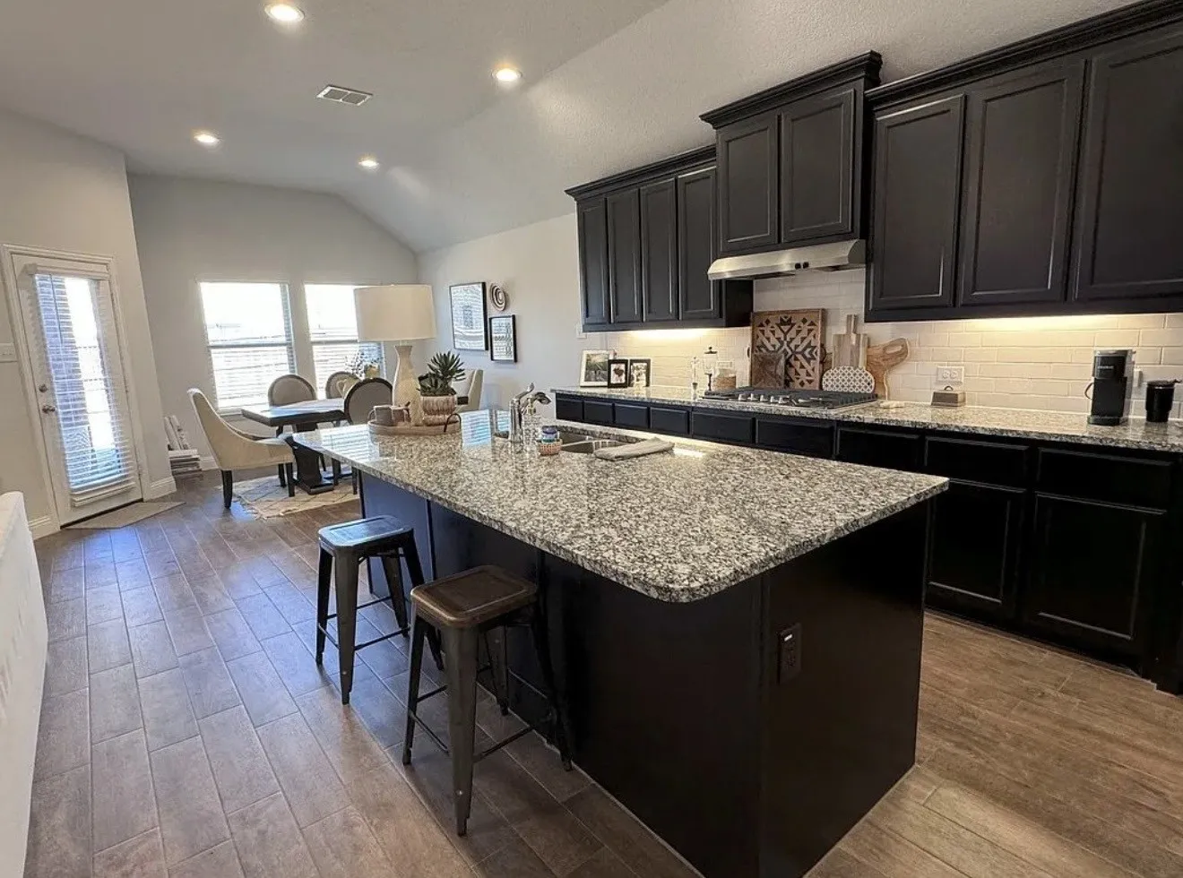 Kitchen island with a granite countertop, dark wood cabinetry, stainless steel range hood, tile backsplash, and wood-finish flooring