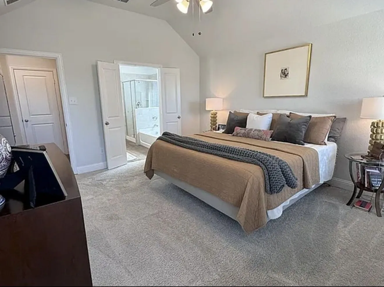 Vaulted ceiling with a ceiling fan, carpet flooring, double doors accessing a bathroom with a shower and soaking tub, and a solid interior door