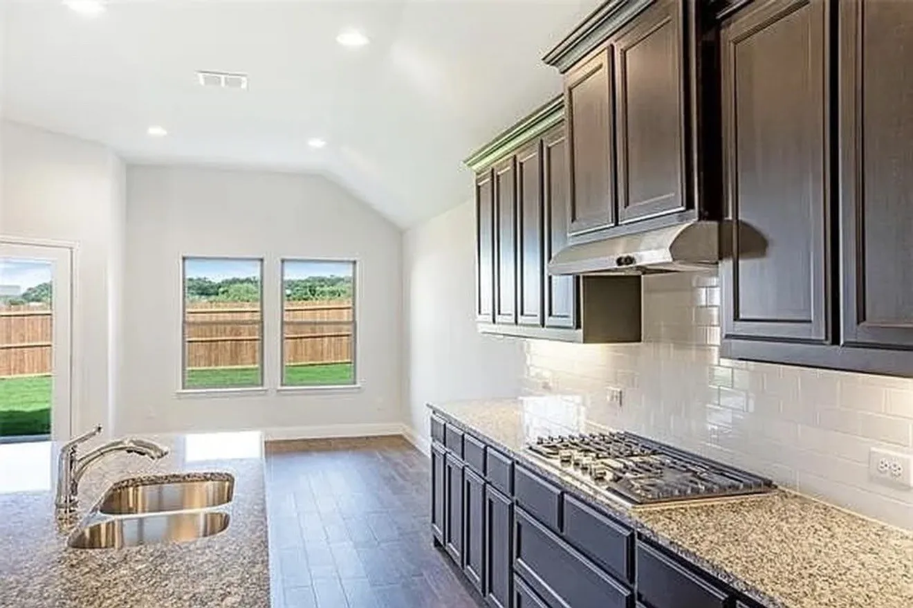 Kitchen with dark wood-finish cabinetry, speckled countertops, subway tile backsplash, and a built-in gas range