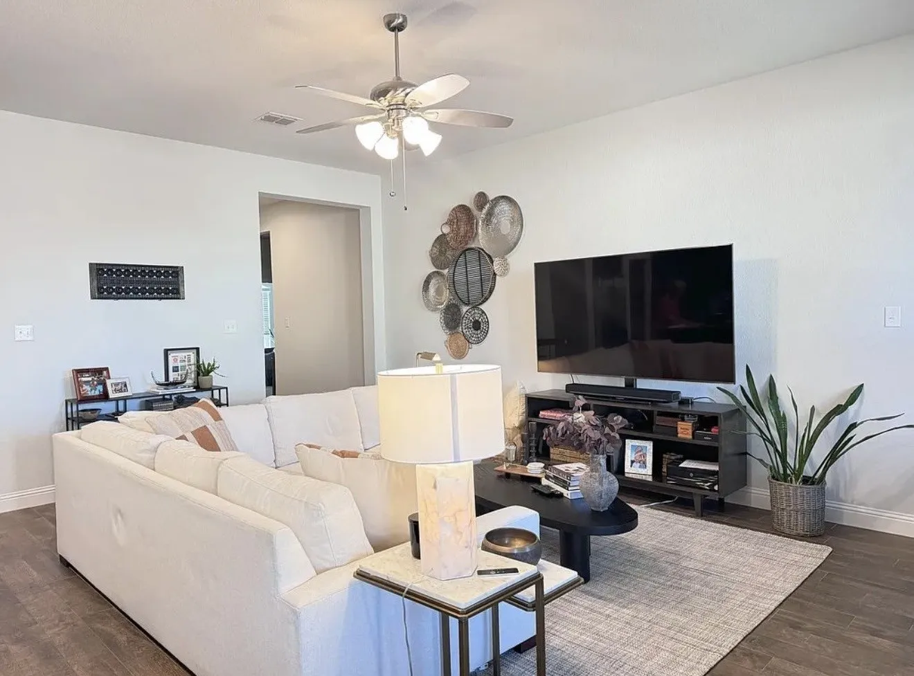Spacious living area featuring wood-finish flooring, a ceiling fan with integrated lighting, and neutral wall tones