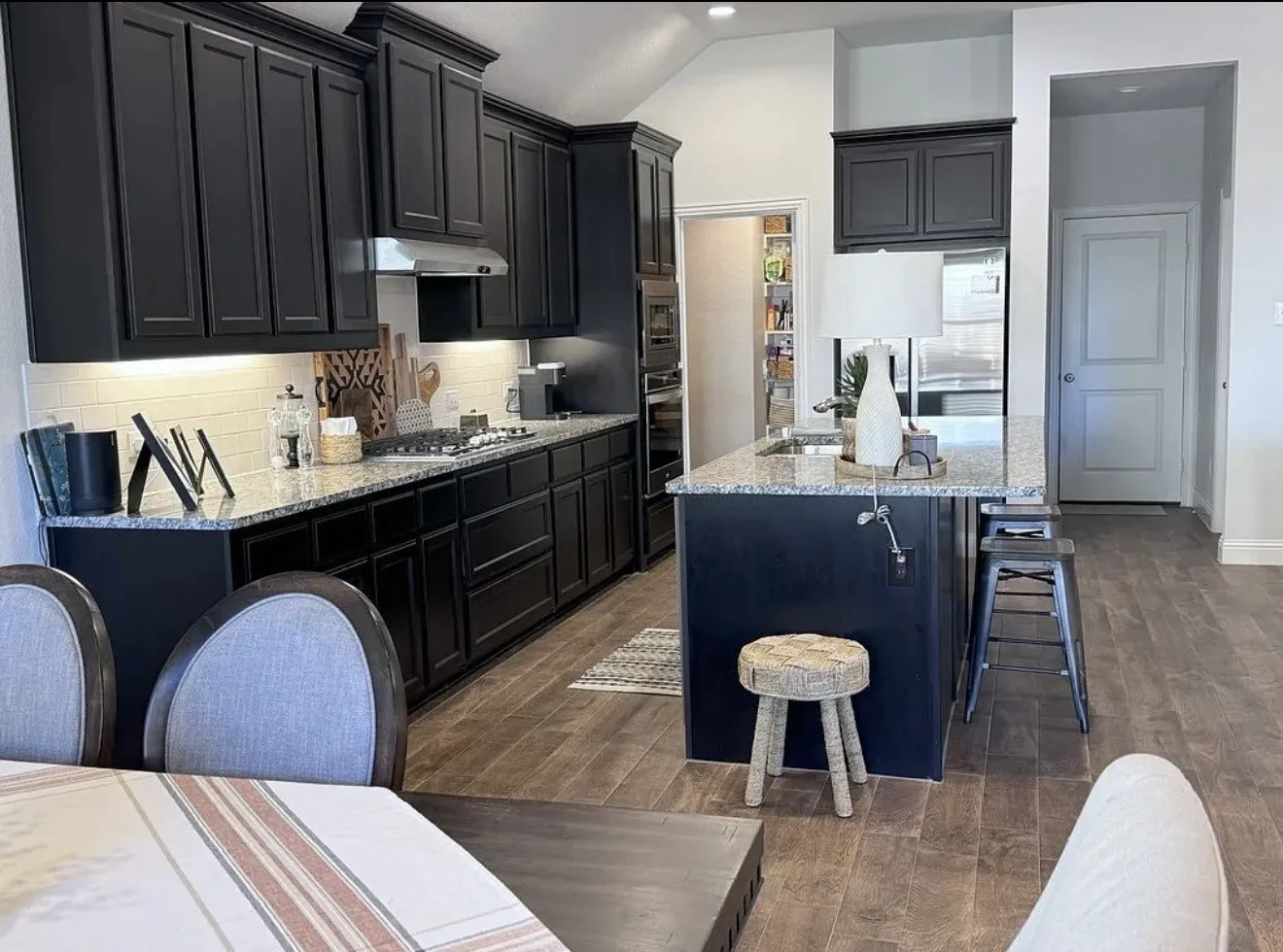 Kitchen featuring dark cabinetry, granite countertops, tile backsplash, a center island with a built-in sink, and wood-finish flooring