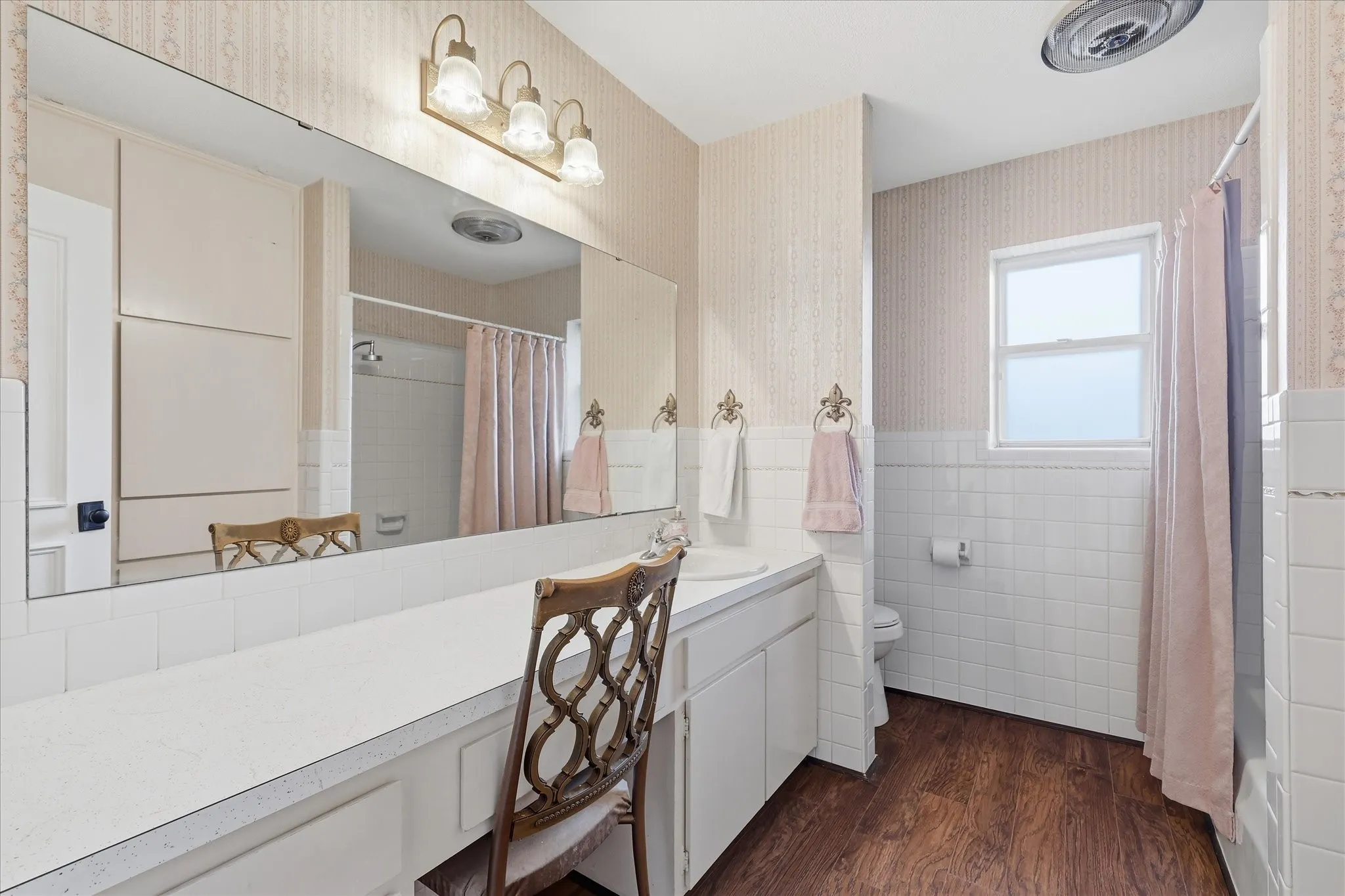 Expansive vanity with integrated storage, white tile wainscoting, and wood-finish flooring