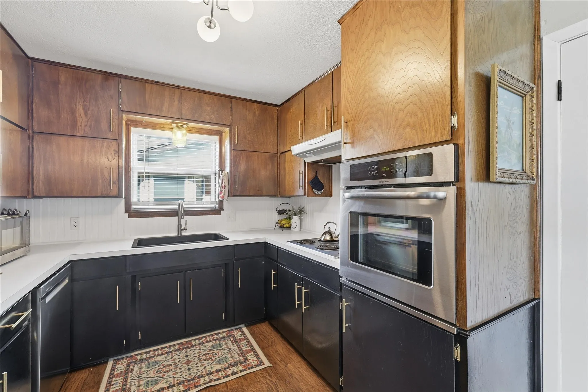 Kitchen featuring a built-in stainless steel oven, white countertops, a black sink with a gooseneck faucet, two-tone cabinetry, and wood-finish flooring