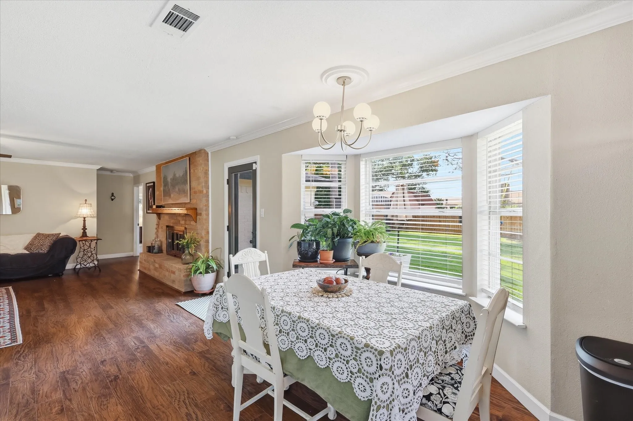 Hardwood-finish flooring, a decorative stone fireplace, crown molding, a bay window with blinds, and a contemporary chandelier