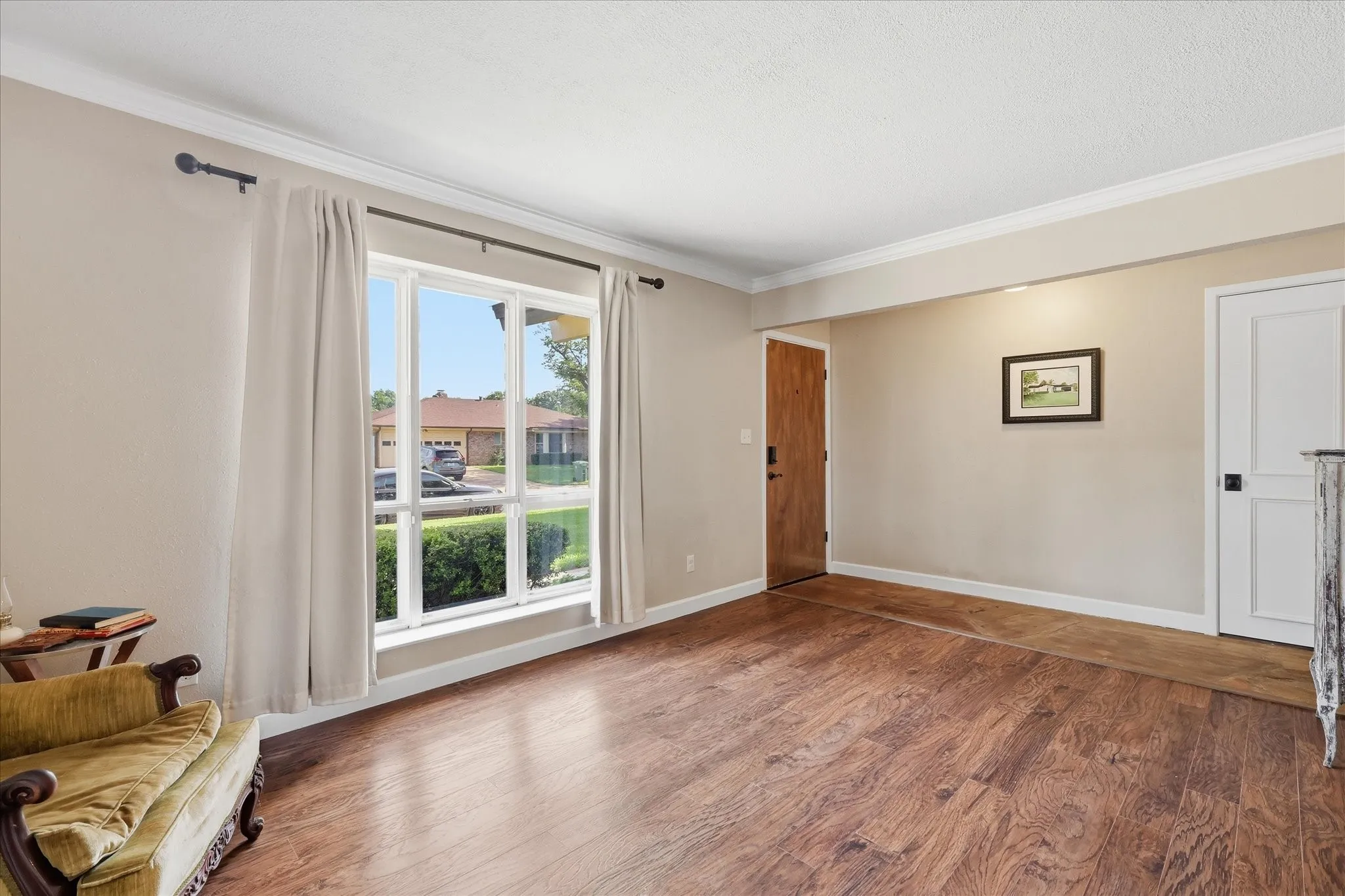 Spacious room with wood-finish flooring, a large multi-pane window, crown molding, and a solid wood entry door