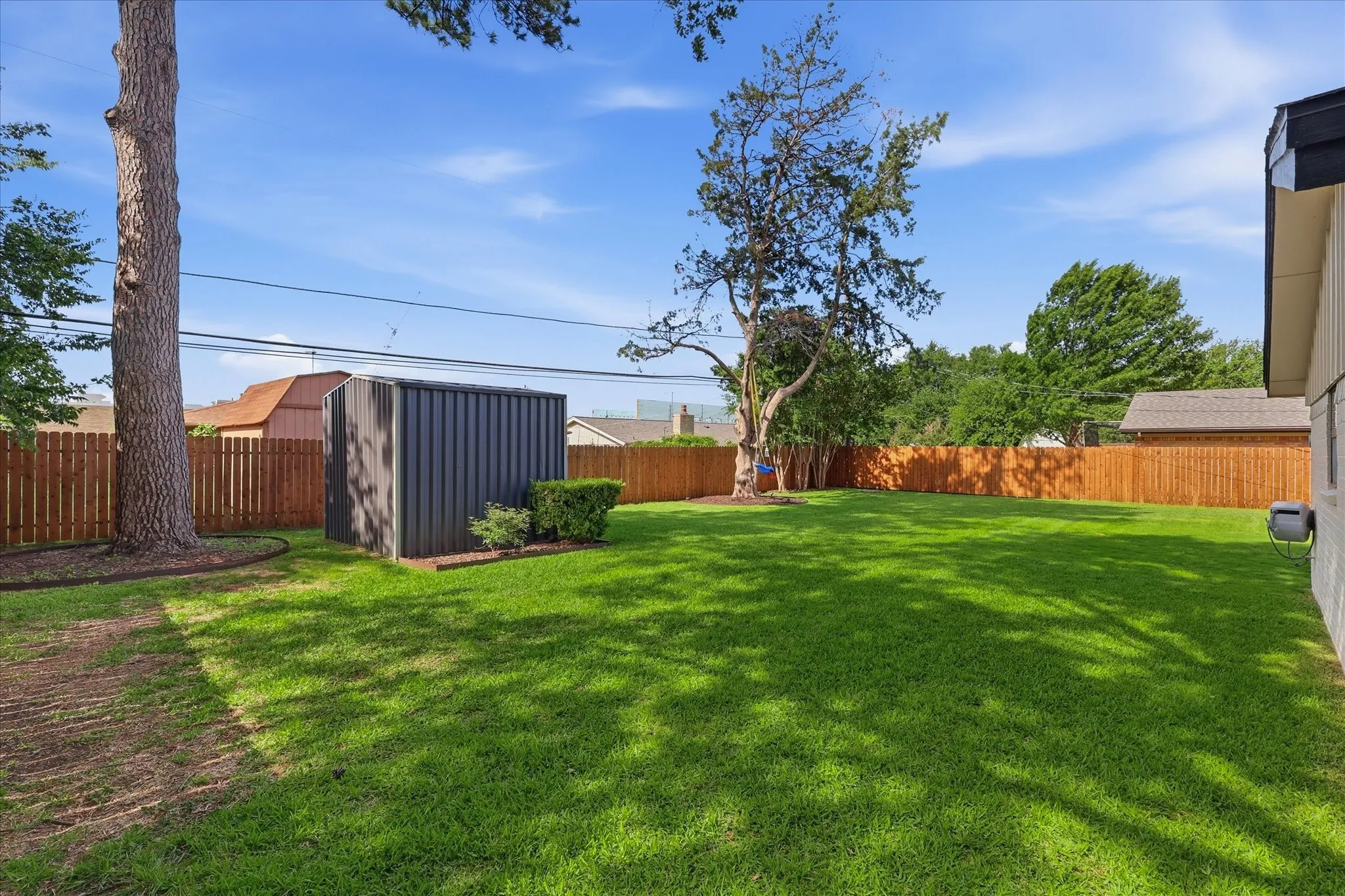 Expansive backyard featuring a privacy fence, mature trees, and a storage shed