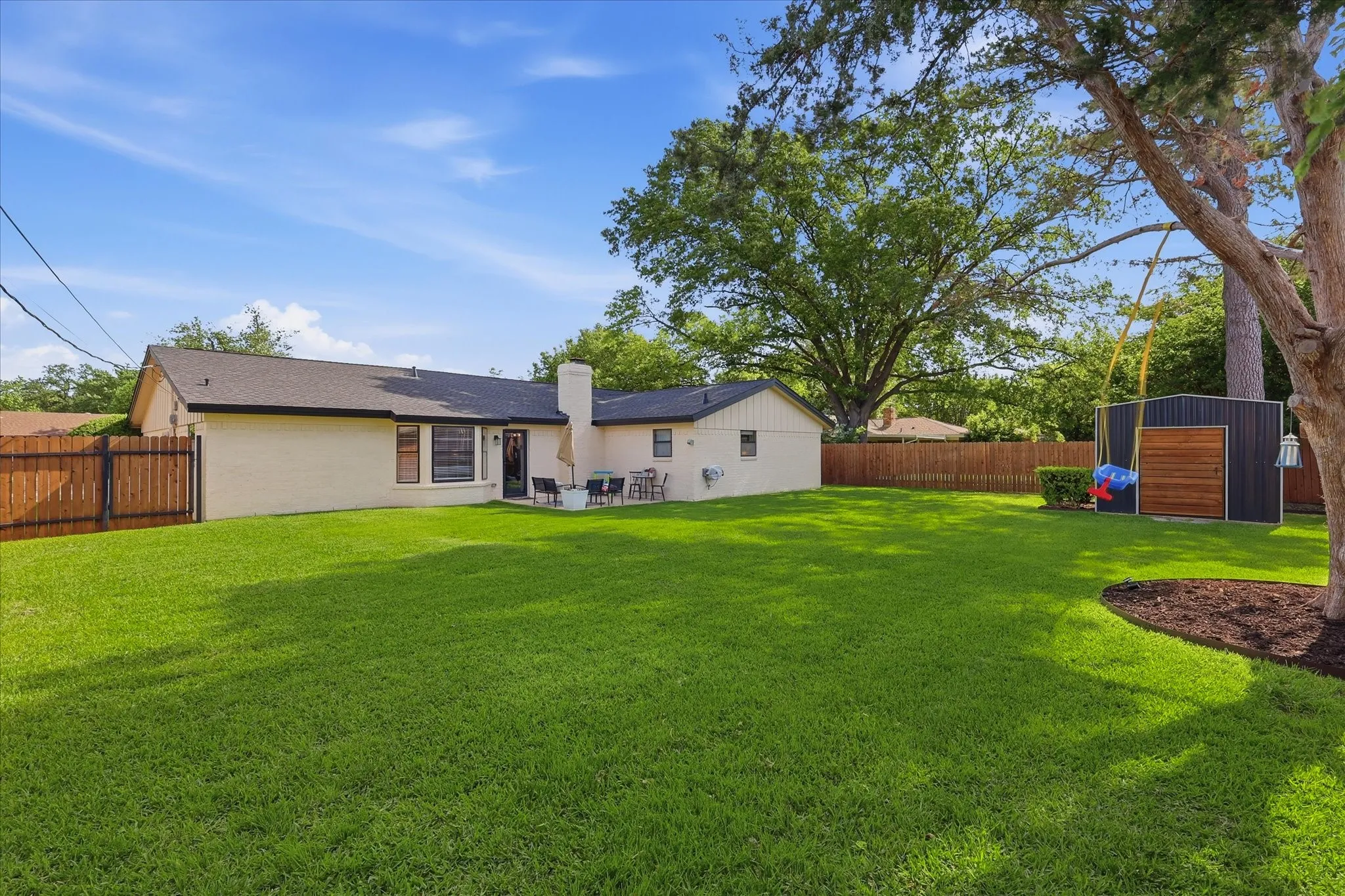 Expansive backyard featuring a manicured lawn, wood privacy fencing, and a dedicated storage shed
