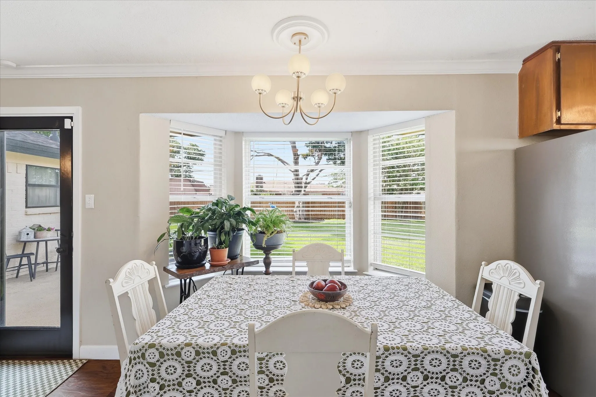 Bay window with horizontal blinds, overhead chandelier light fixture, crown molding, and wood-finish flooring