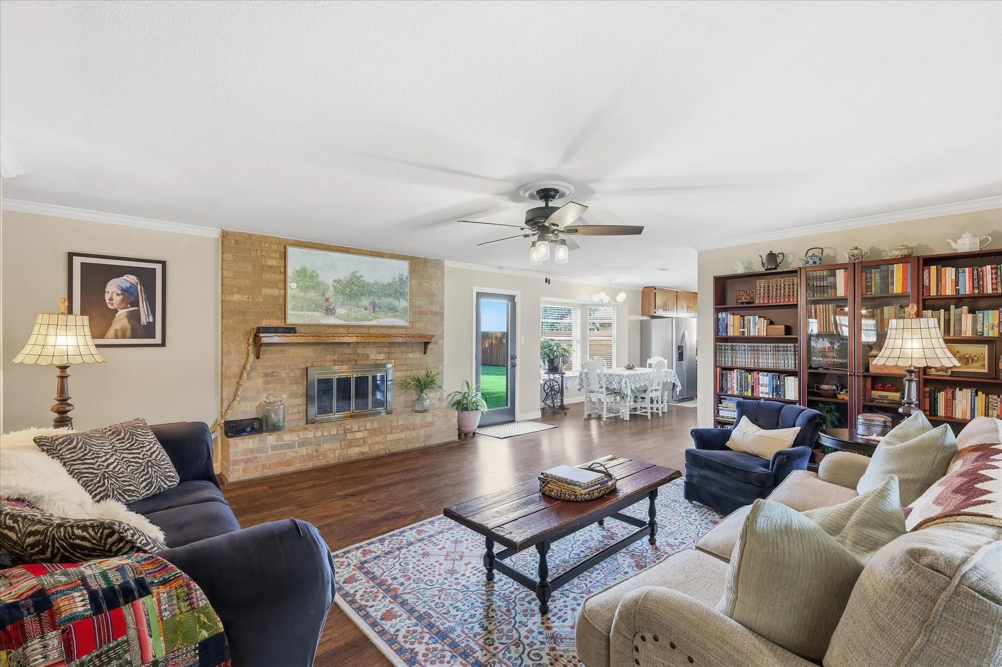 Living area with wood-finish flooring, brick-surround fireplace, built-in shelving, and crown molding