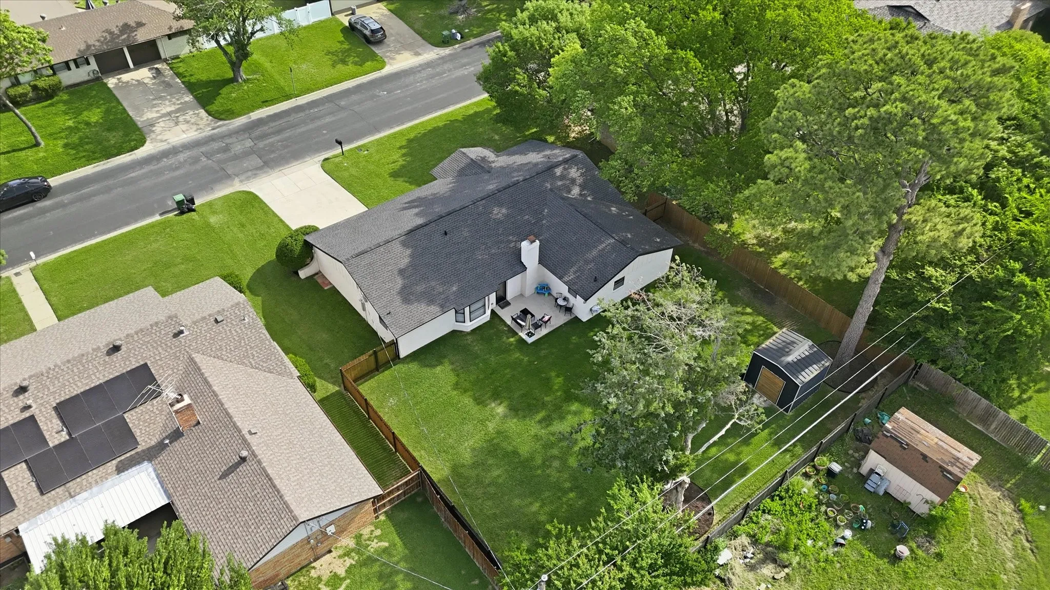 Expansive fenced backyard with a patio area, mature trees, and a storage shed