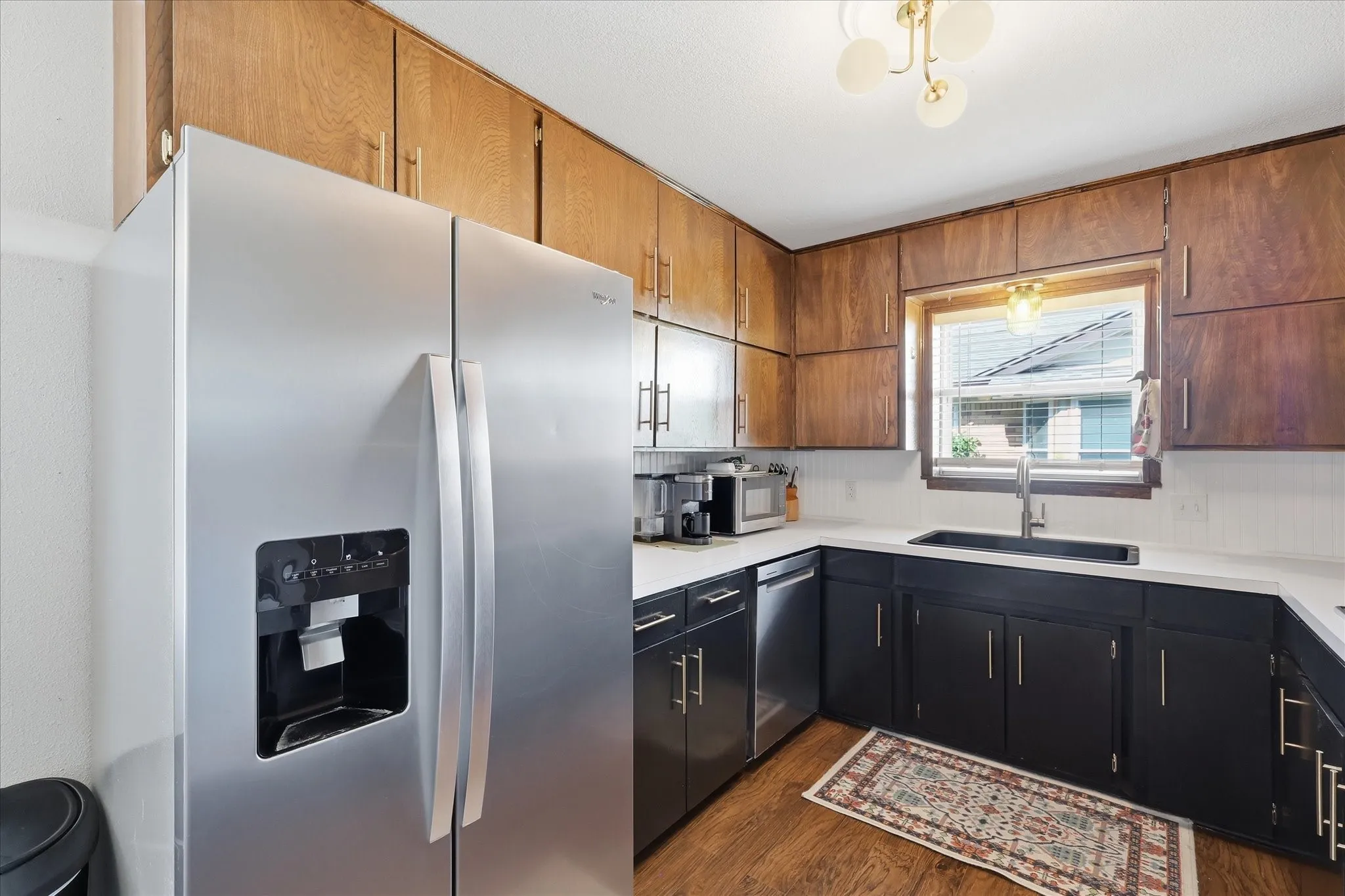 Kitchen featuring wood-finish upper cabinetry, stainless steel side-by-side refrigerator, dark-finish lower cabinetry, white countertops, and a stainless steel dishwasher
