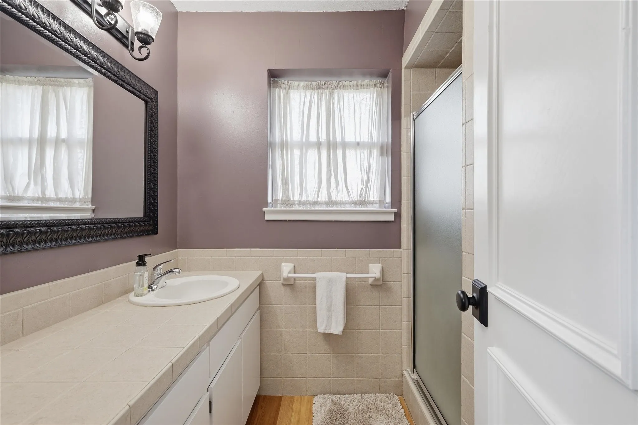 White vanity with an integrated sink, polished chrome faucet, full-width wall mirror, and an enclosed shower with a frosted glass panel