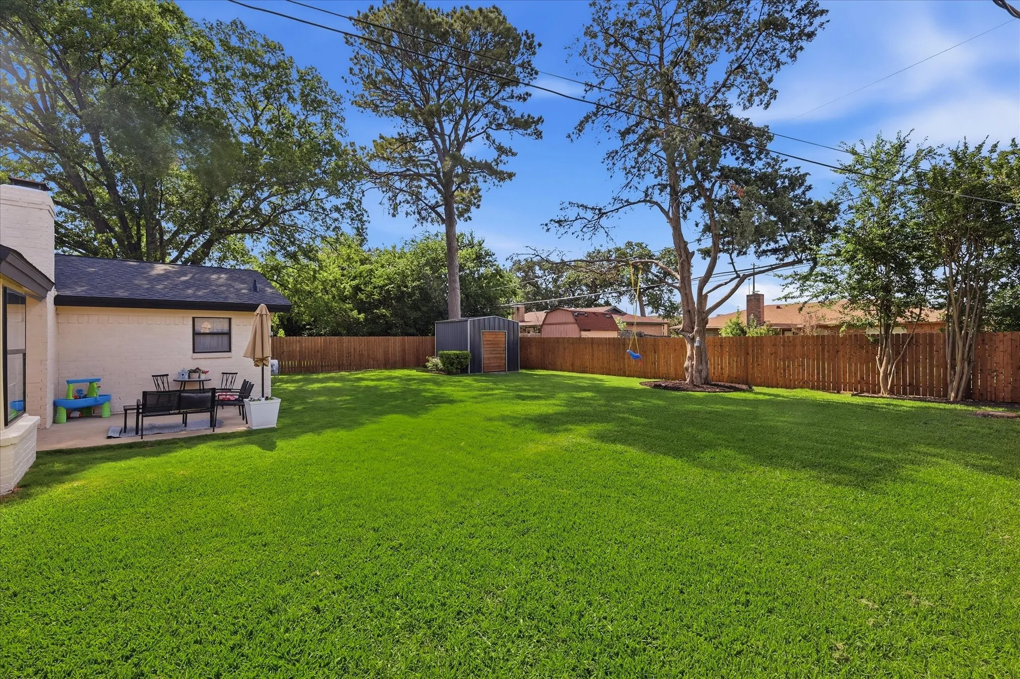 Expansive green lawn, private wood fence, mature trees, and a patio area