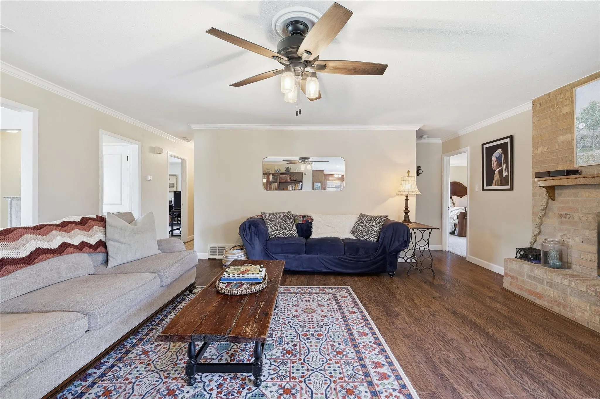 Wood-finish flooring, crown molding, ceiling fan with integrated lighting, recessed lighting, and a brick fireplace
