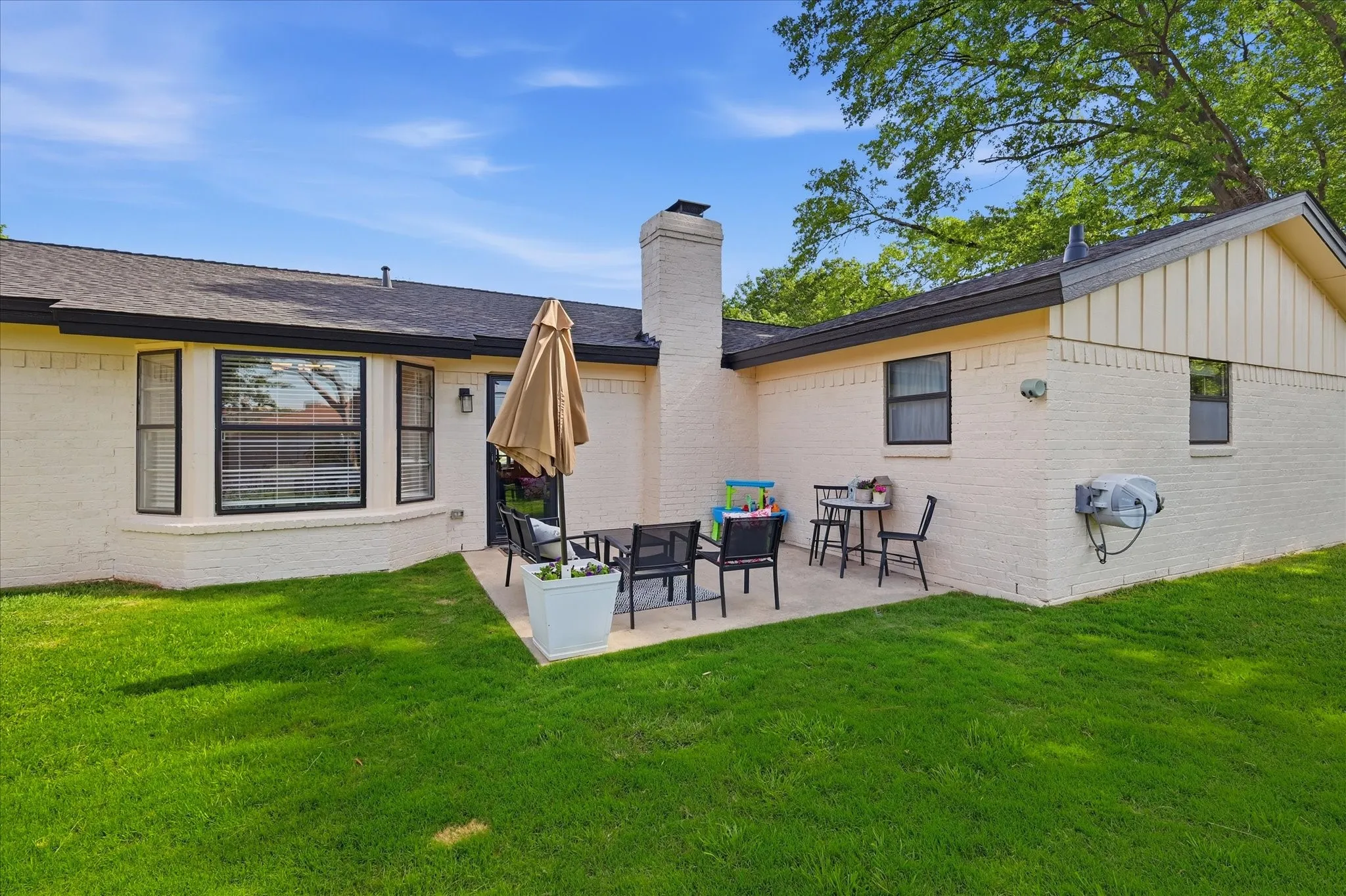Expansive lawn with a concrete patio, brick exterior, bay window, and a prominent chimney