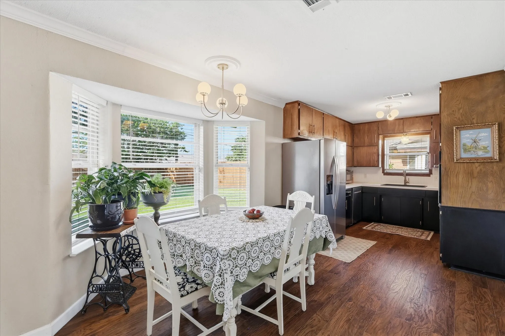 Wood-finish flooring, bay window, upper wood cabinetry, lower black cabinetry, and a modern chandelier