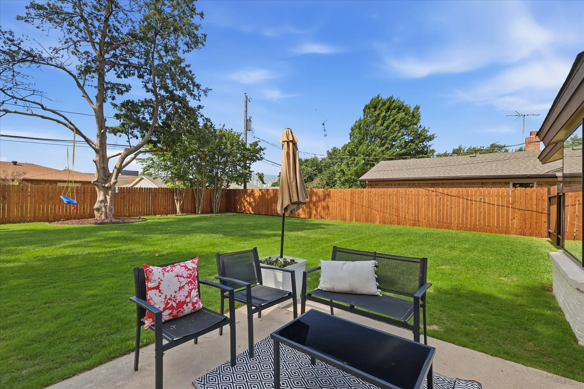 Expansive backyard with a manicured lawn, established shade trees, and a wood privacy fence