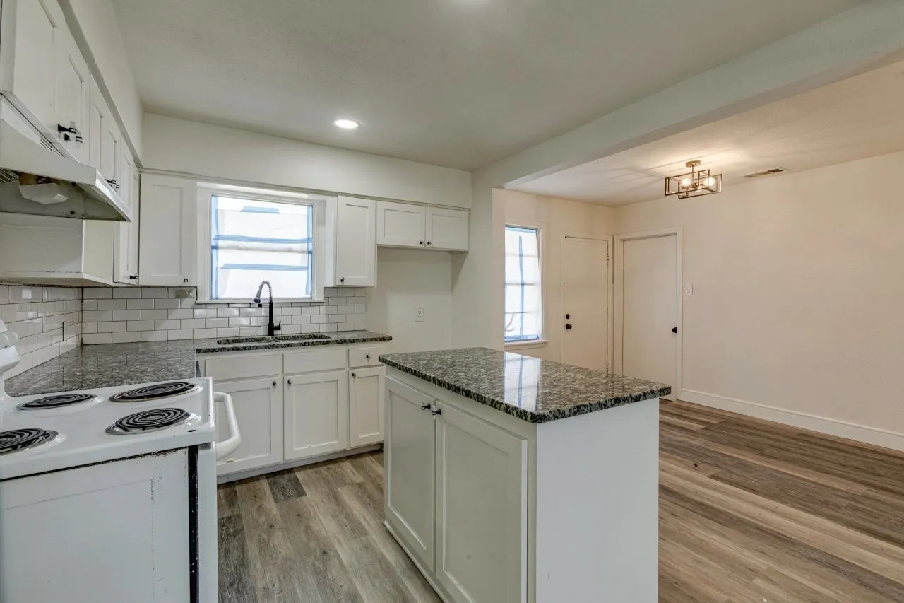 Kitchen featuring white cabinetry, subway tile backsplash, dark countertops, an island, and wood-finish flooring
