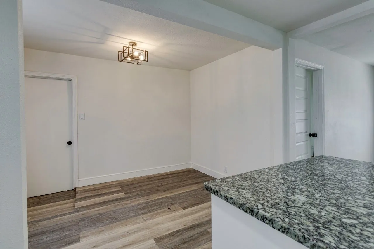 Granite countertop, wood-finish flooring, white walls, and a contemporary ceiling light fixture