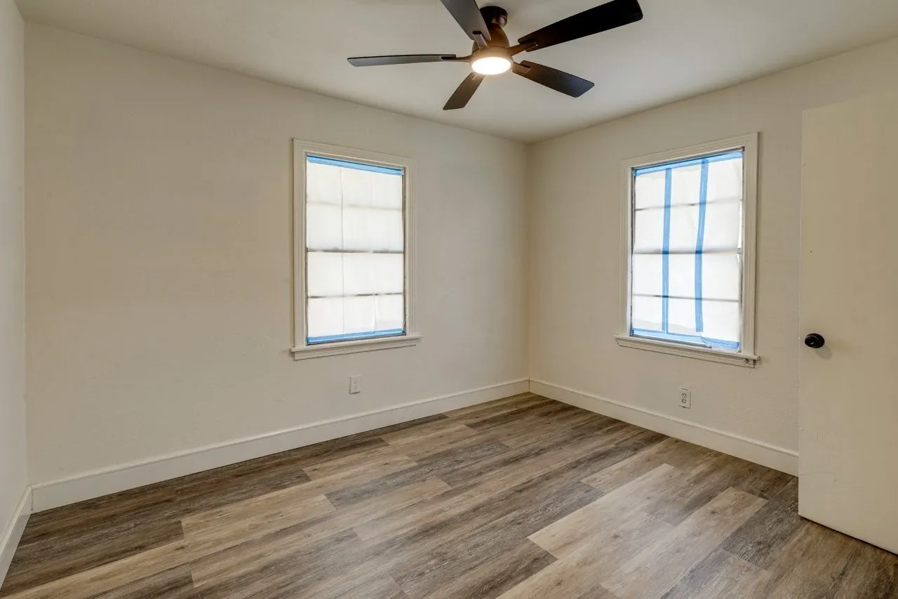Wood-finish flooring, two windows with white trim, and a ceiling fan with integrated lighting
