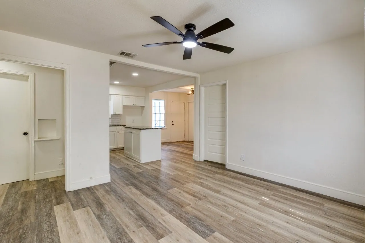 Wood-finish flooring, recessed lighting, ceiling fan, white cabinetry, and a kitchen island with a dark countertop