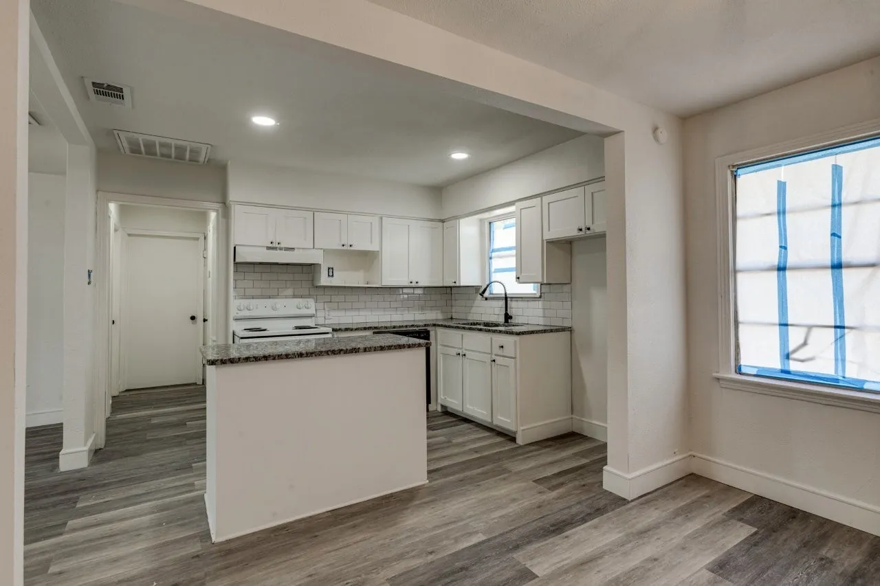 Kitchen featuring white shaker cabinetry, subway tile backsplash, granite-style countertops, and wood-finish flooring