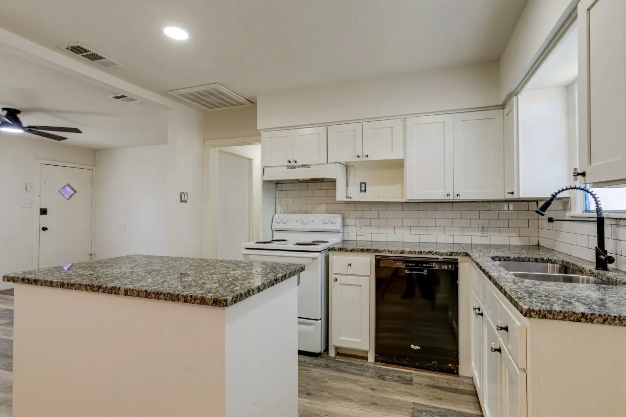 Kitchen featuring a center island with granite countertop, white cabinetry, subway tile backsplash, and wood-finish flooring