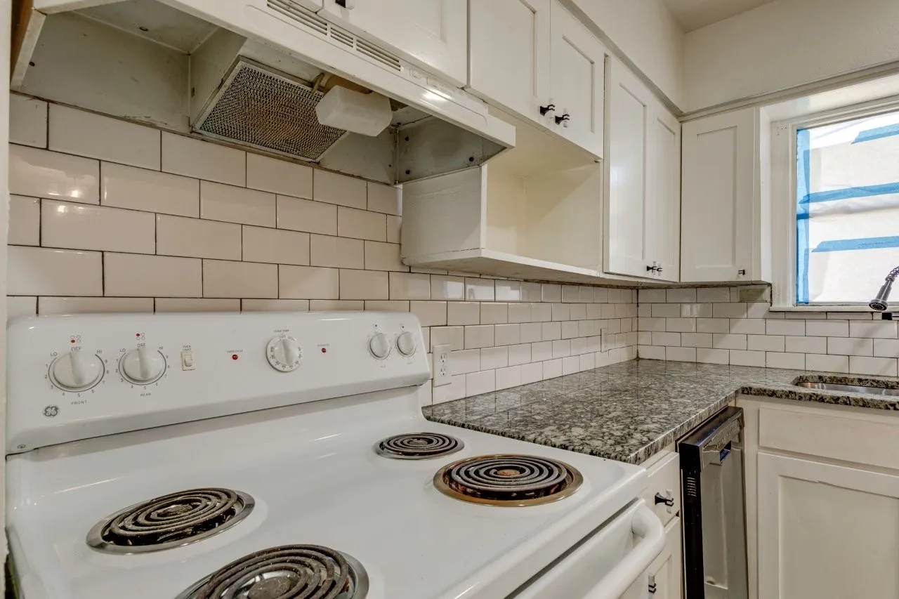 White cabinetry, granite countertops, subway tile backsplash, and a built-in range hood