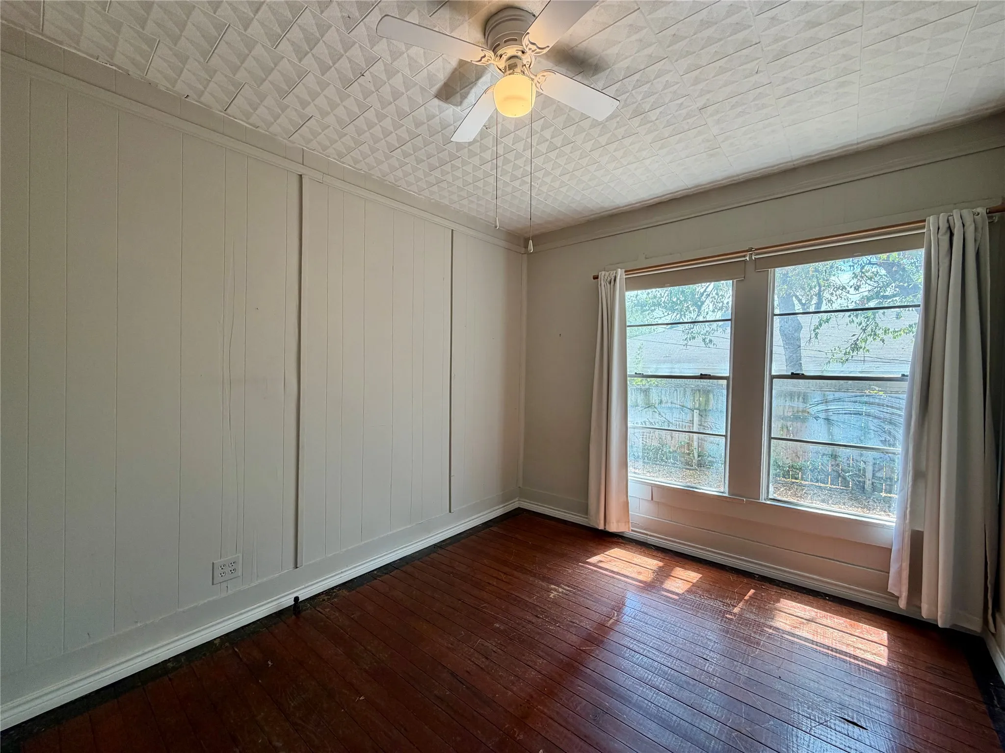 Wood-finish flooring, paneled walls, dual windows, textured ceiling, and a ceiling fan