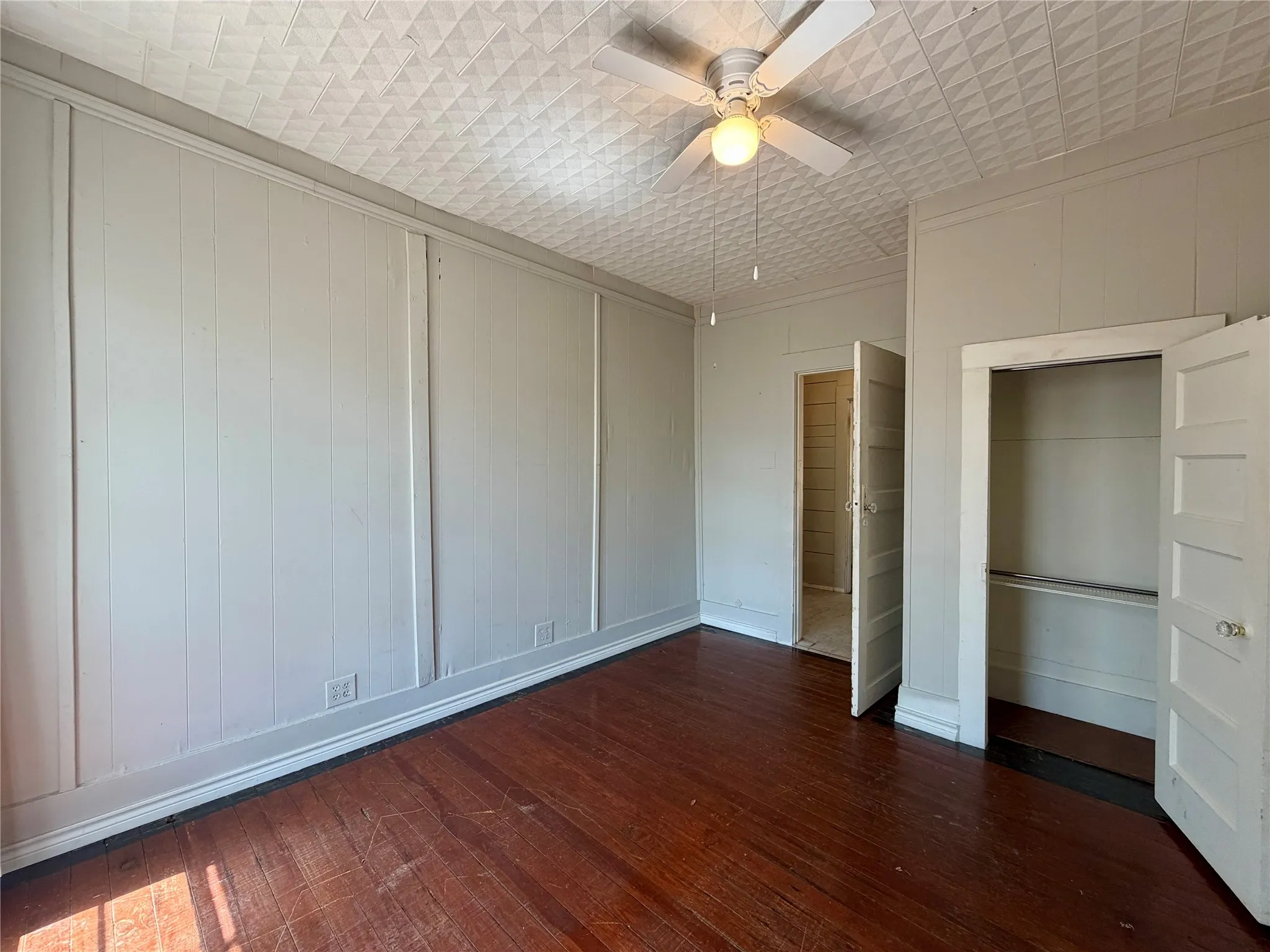 Hardwood flooring, textured ceiling, ceiling fan with light fixture, board and batten wall detailing, and built-in closet with double doors