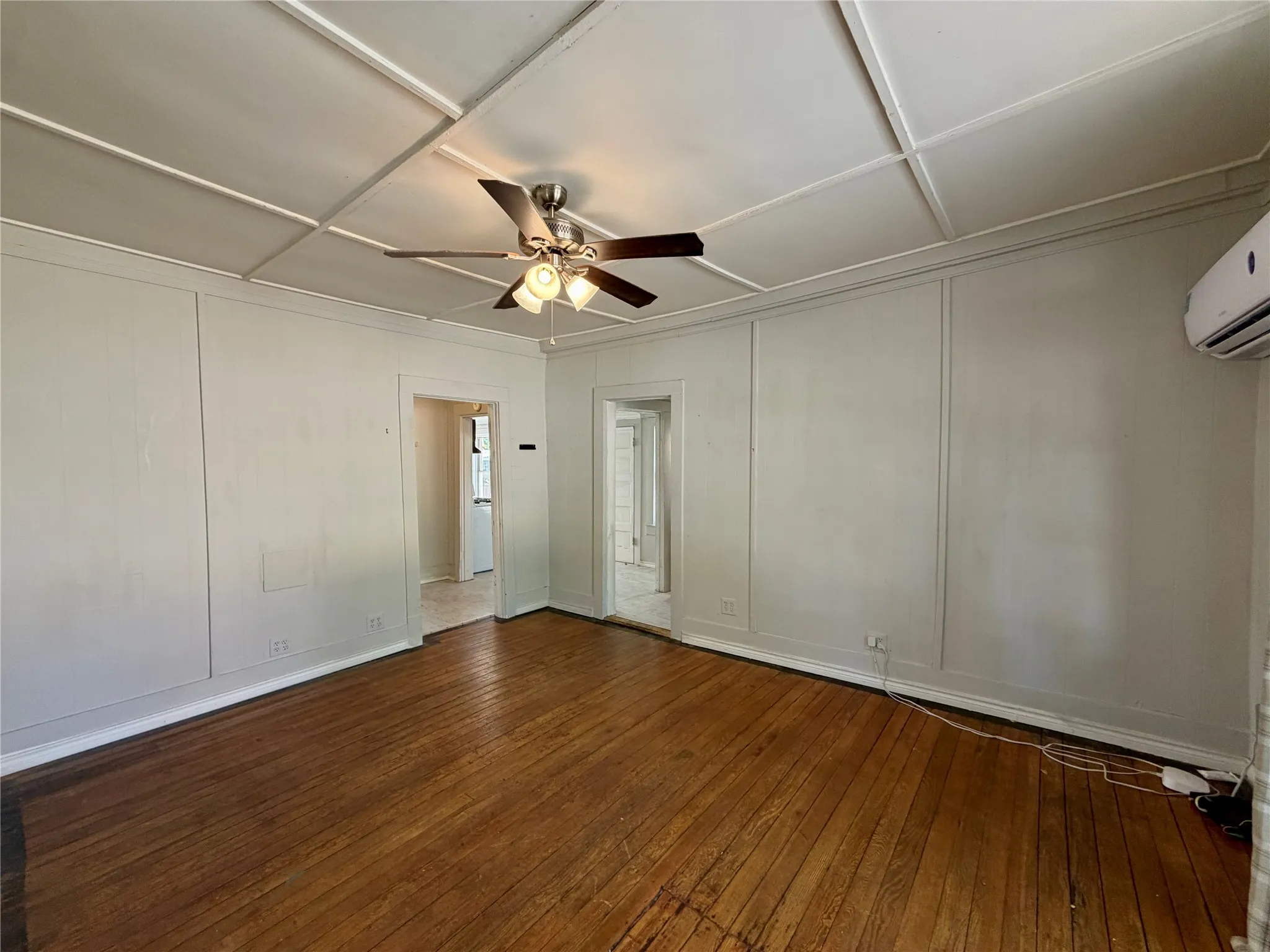 Hardwood flooring, coffered ceiling, ceiling fan, wall paneling, and split-system AC unit
