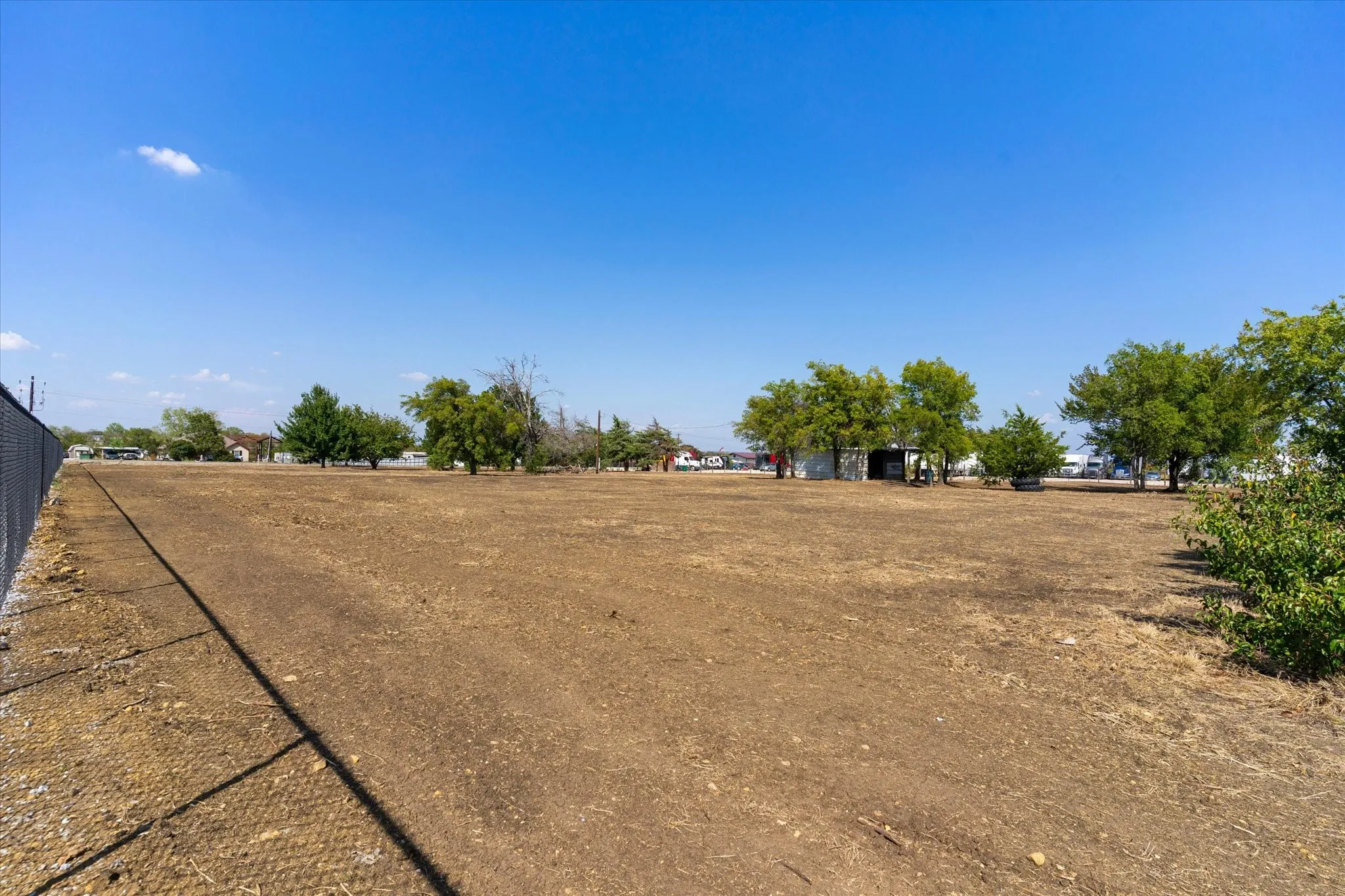 Expansive unimproved lot featuring a chain-link fence border and scattered mature trees