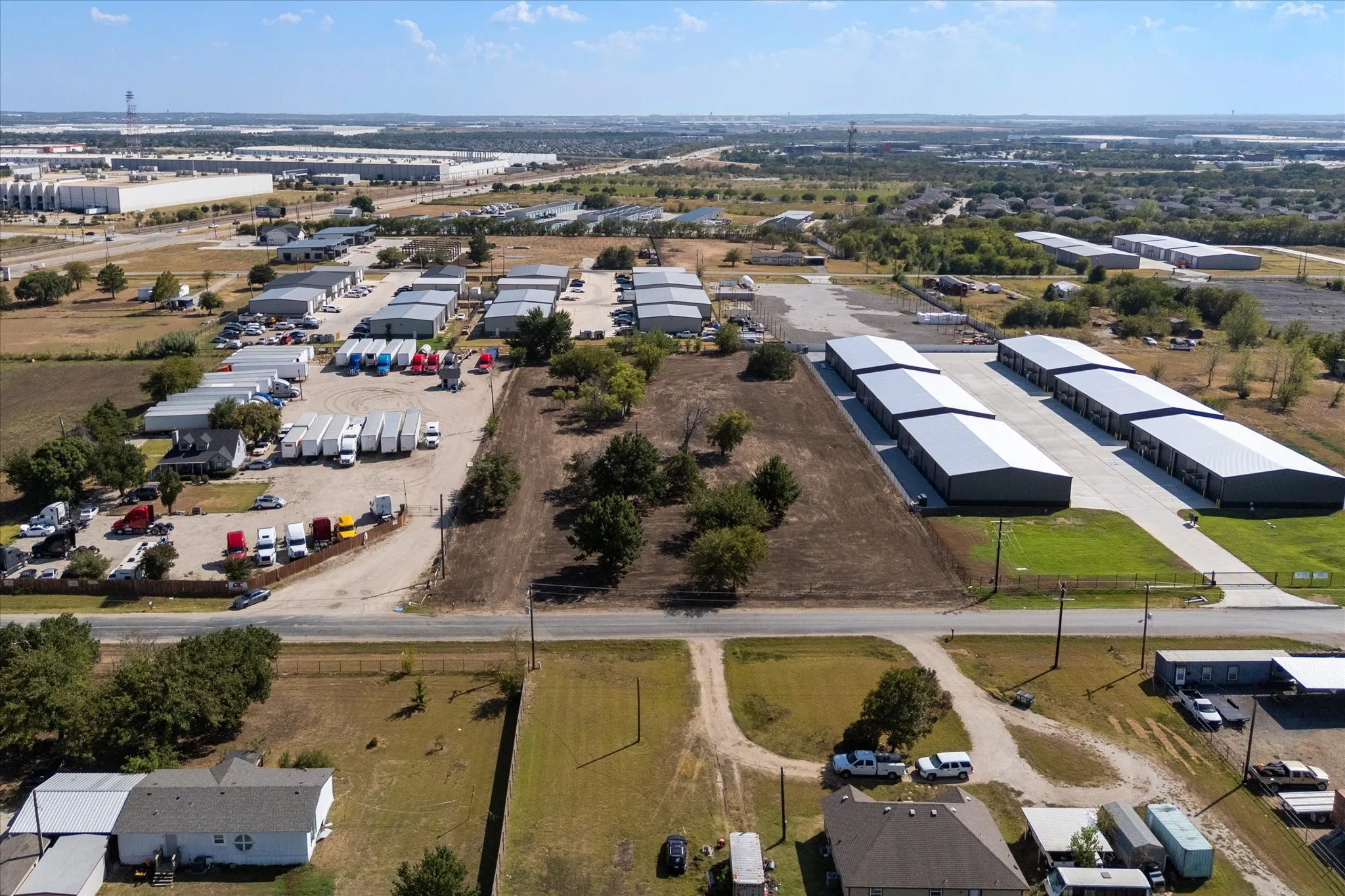 Multiple commercial buildings with metal roofs, paved access roads, and undeveloped land