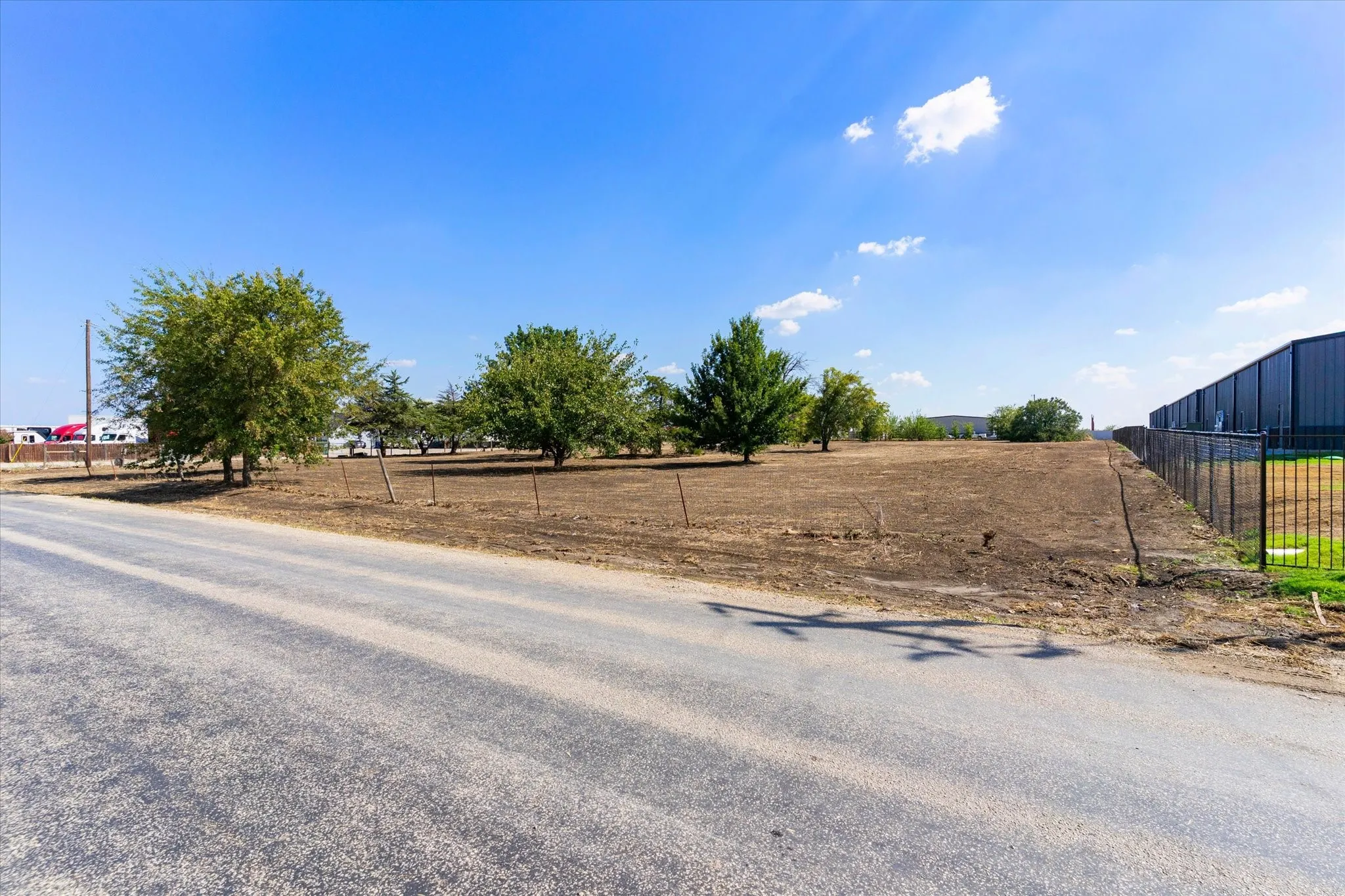Expansive lot featuring mature trees, a perimeter fence, and direct paved road frontage